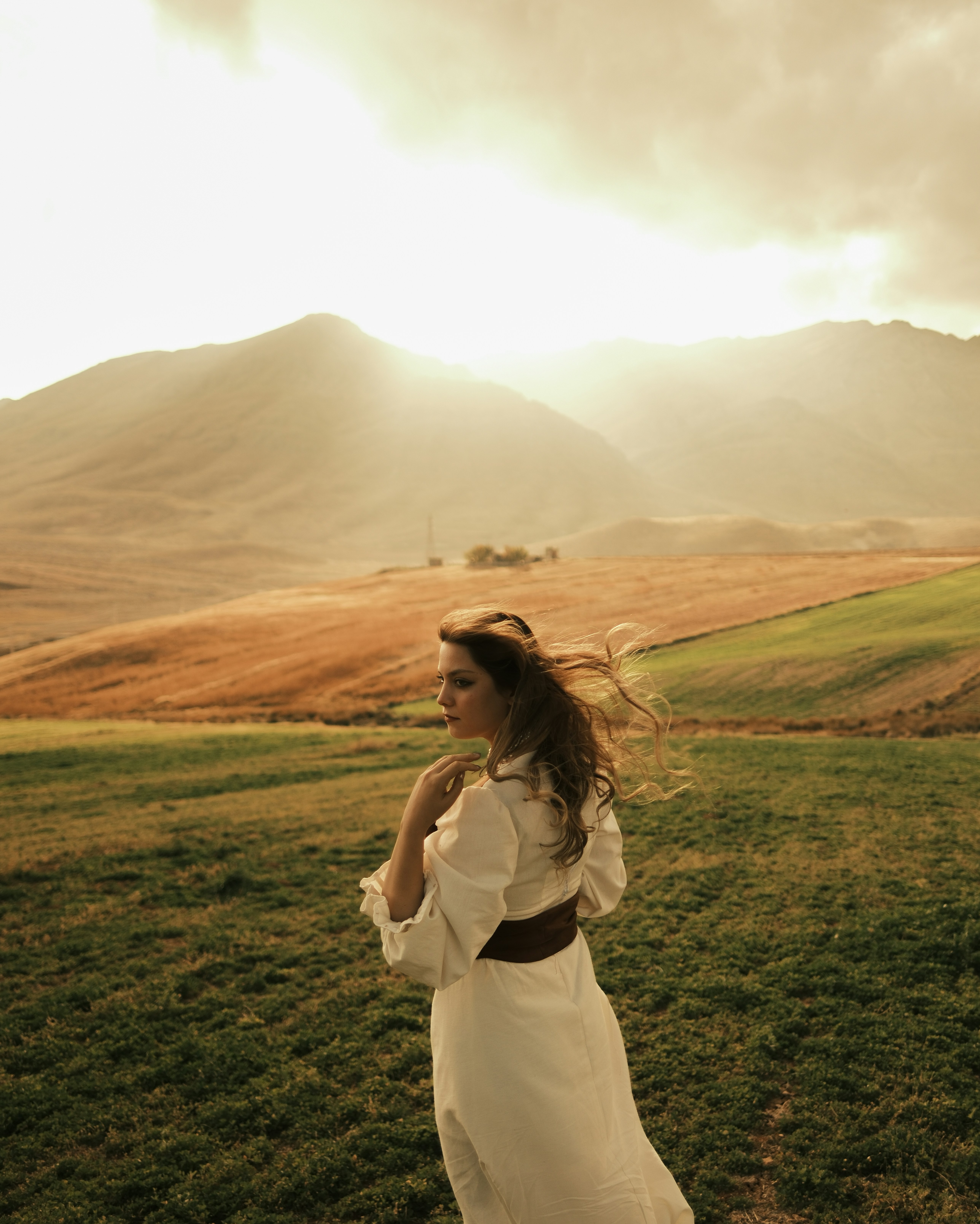 Woman in white dress in a grassy field with mountains.