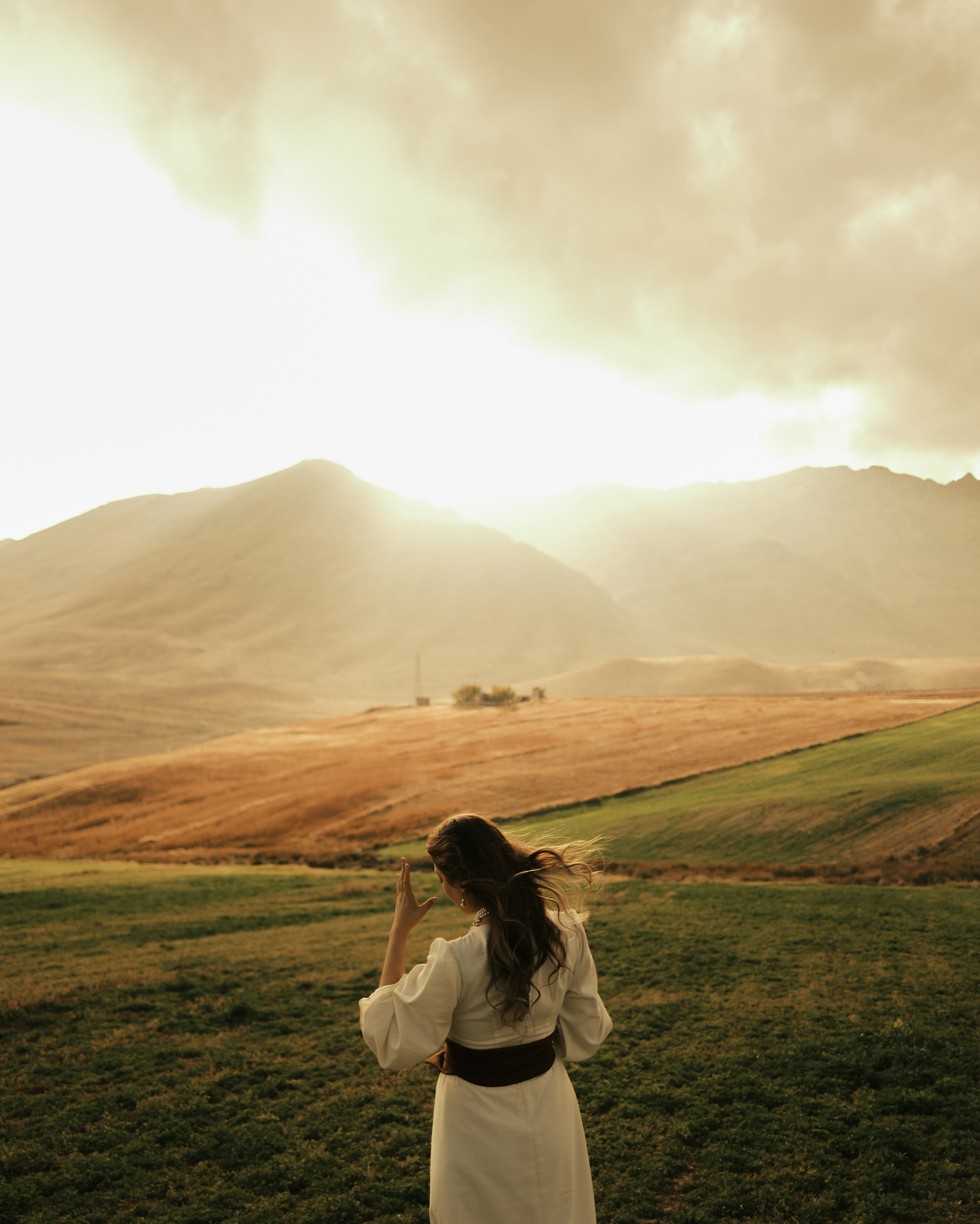 Woman in white dress facing mountains at sunset