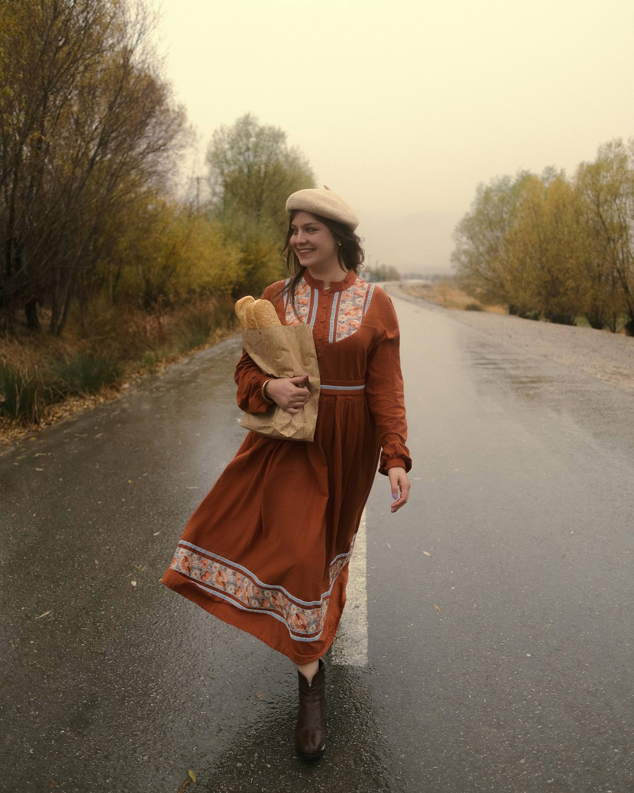 Woman in dress walks on wet road with bag.