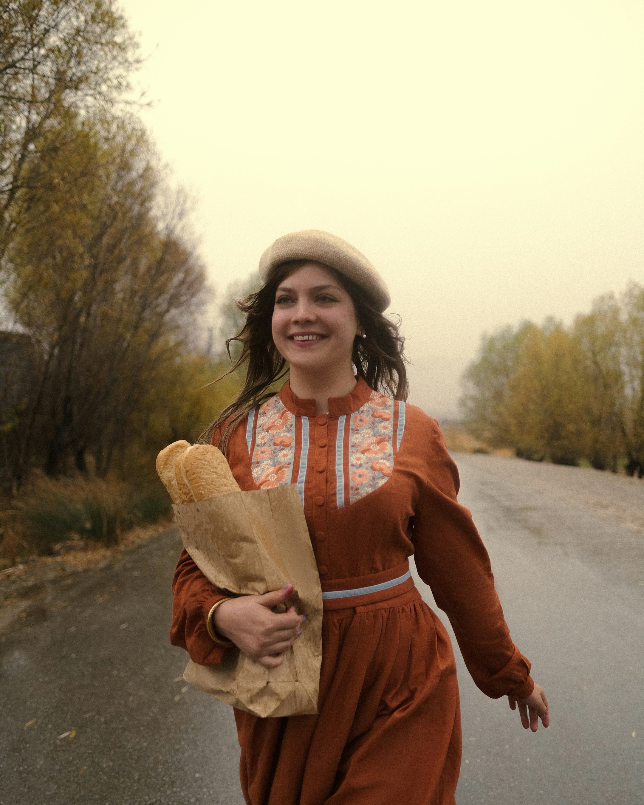 Woman in beret carrying baguettes on country road