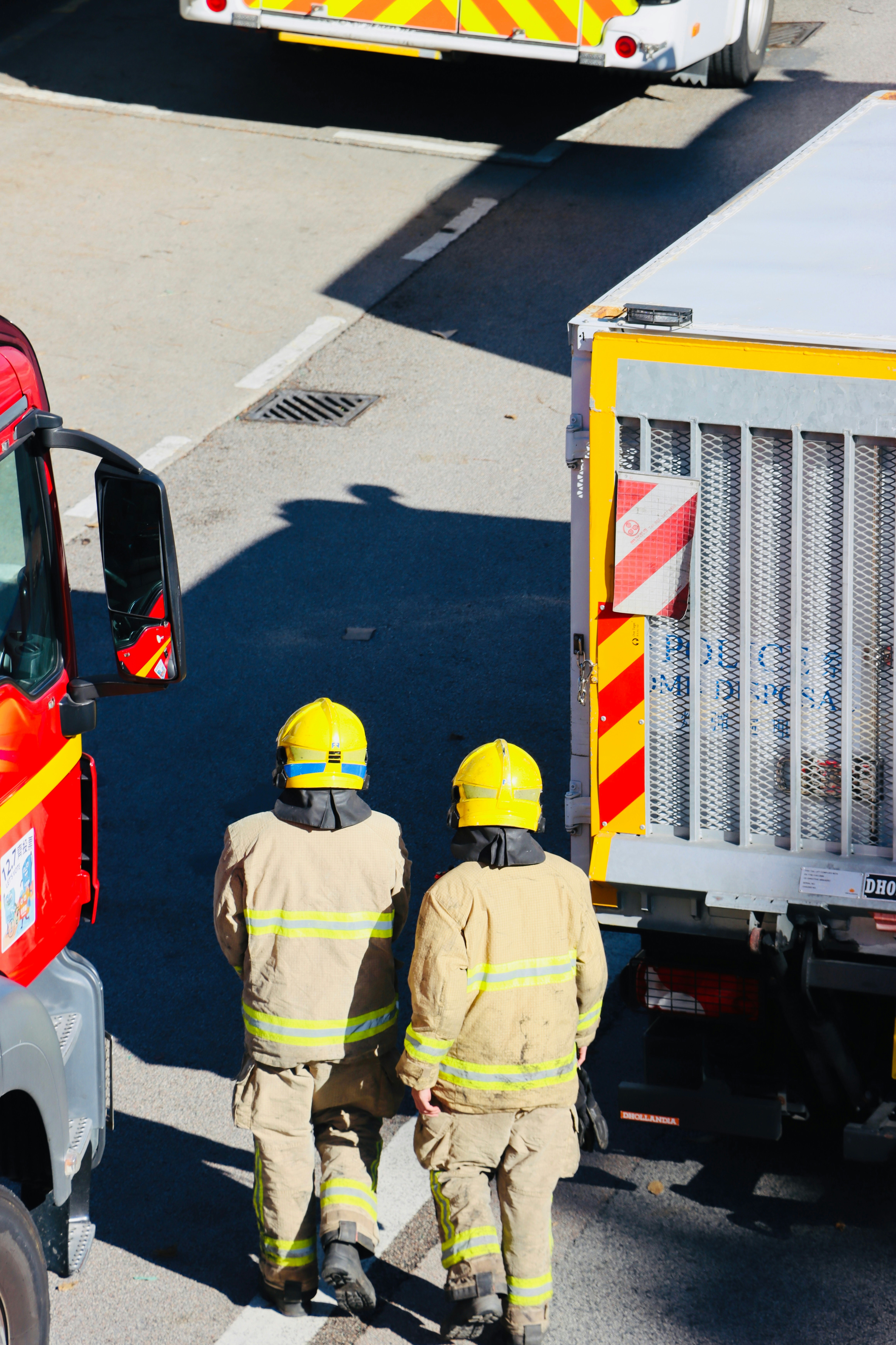Two firefighters in yellow helmets walk near trucks.