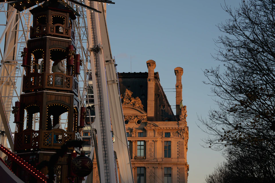 A giant Ferris wheel illuminated at dusk beside an ornate Paris building, the centrepiece of the Tuileries Christmas market
