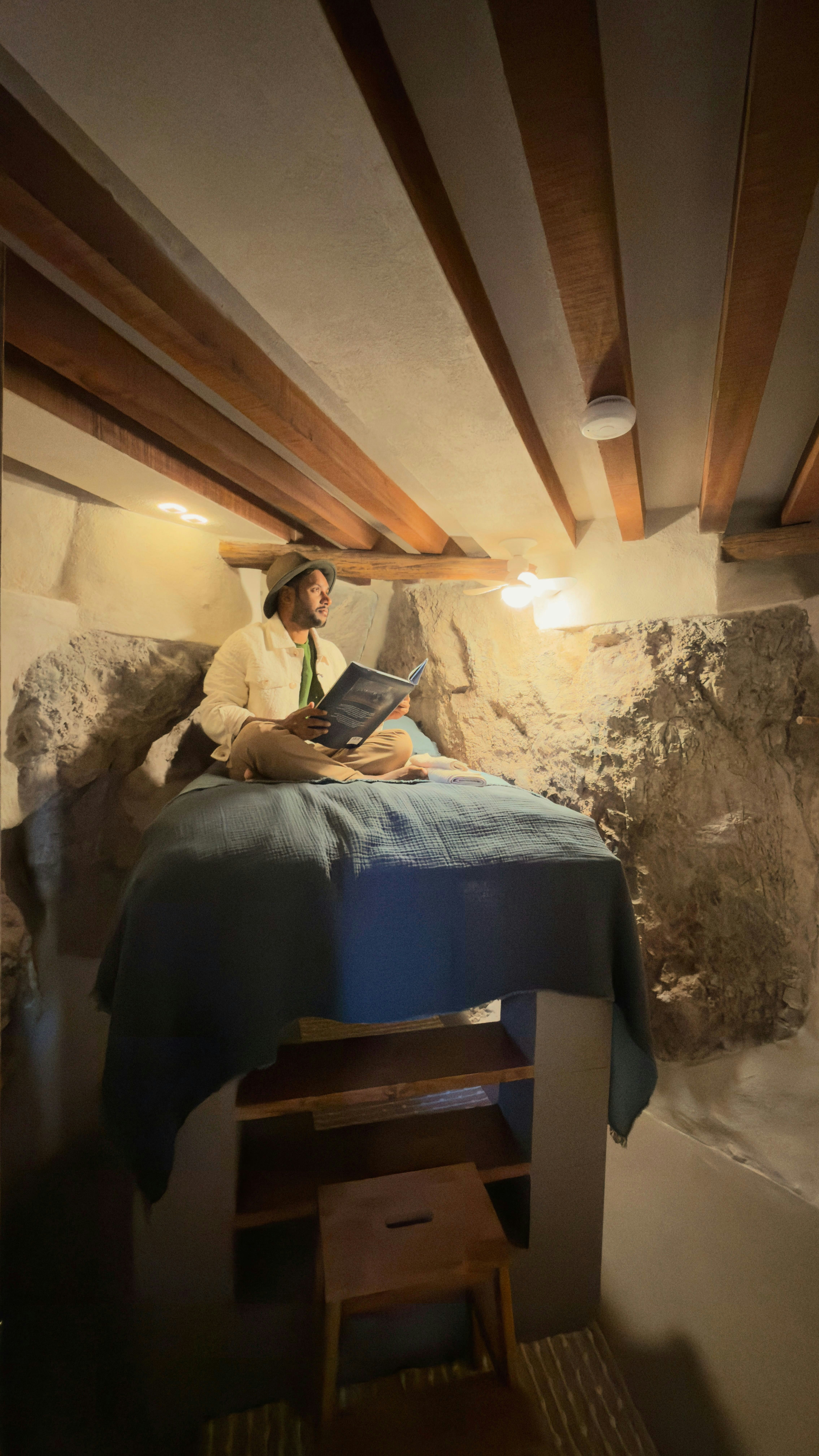 A person sits reading a book on a bed.