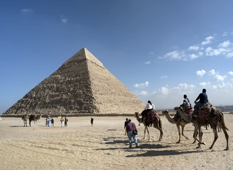 People on a guided tour riding camels near the great pyramid of giza.
