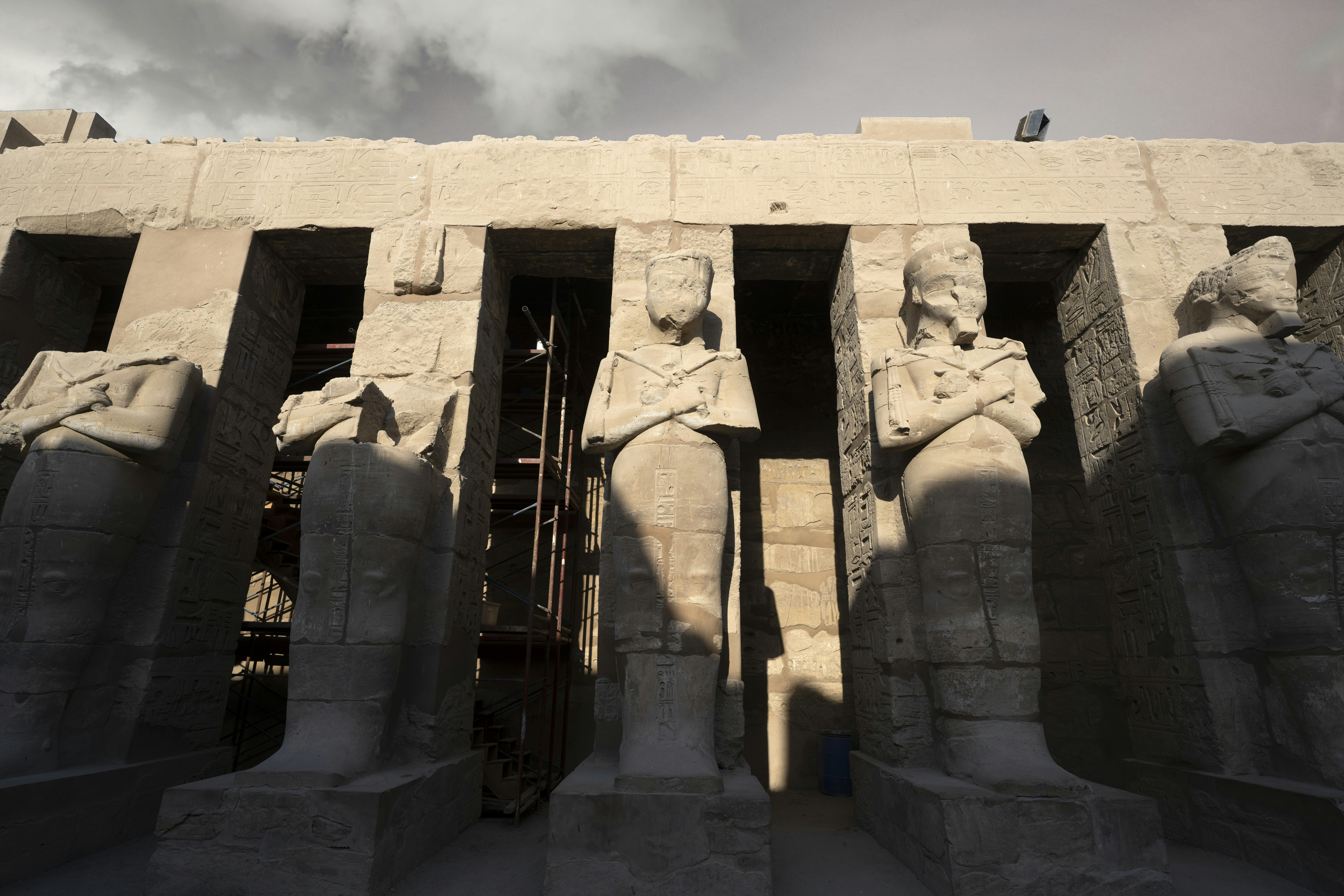 Ancient egyptian statues line a stone temple facade.