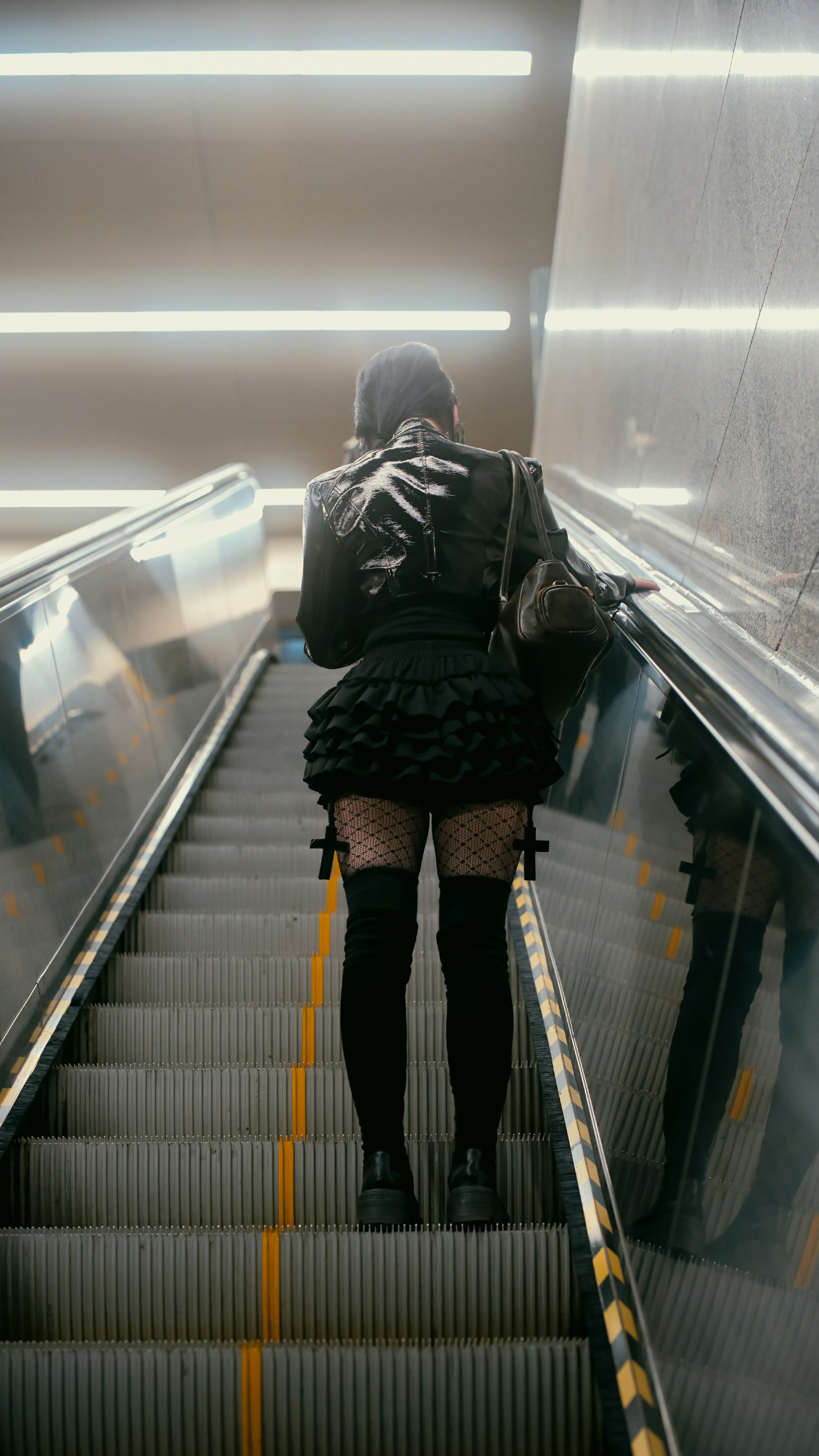 Mujer con traje gótico negro en la escalera mecánica