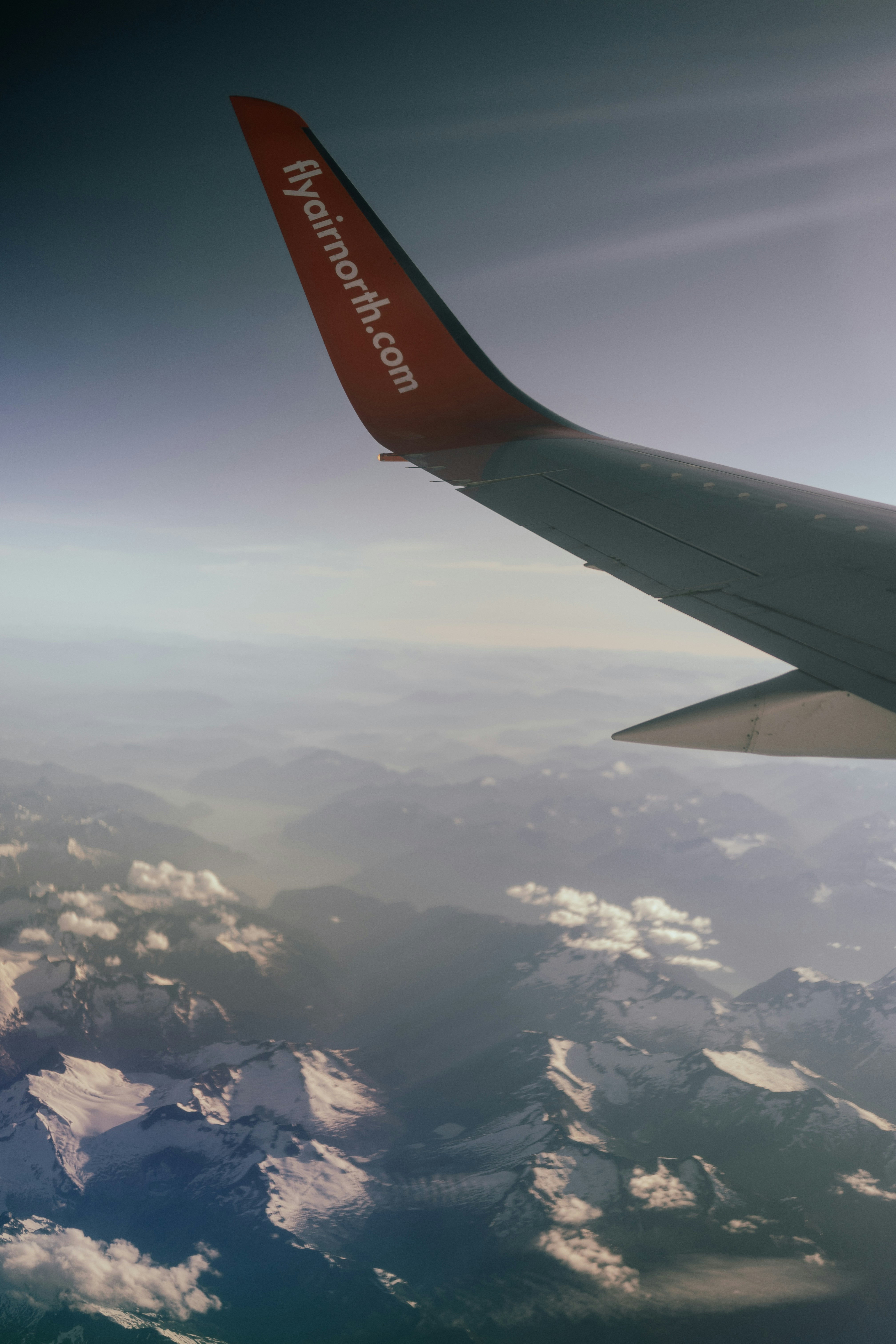 Airplane wing over snowy mountains during daytime