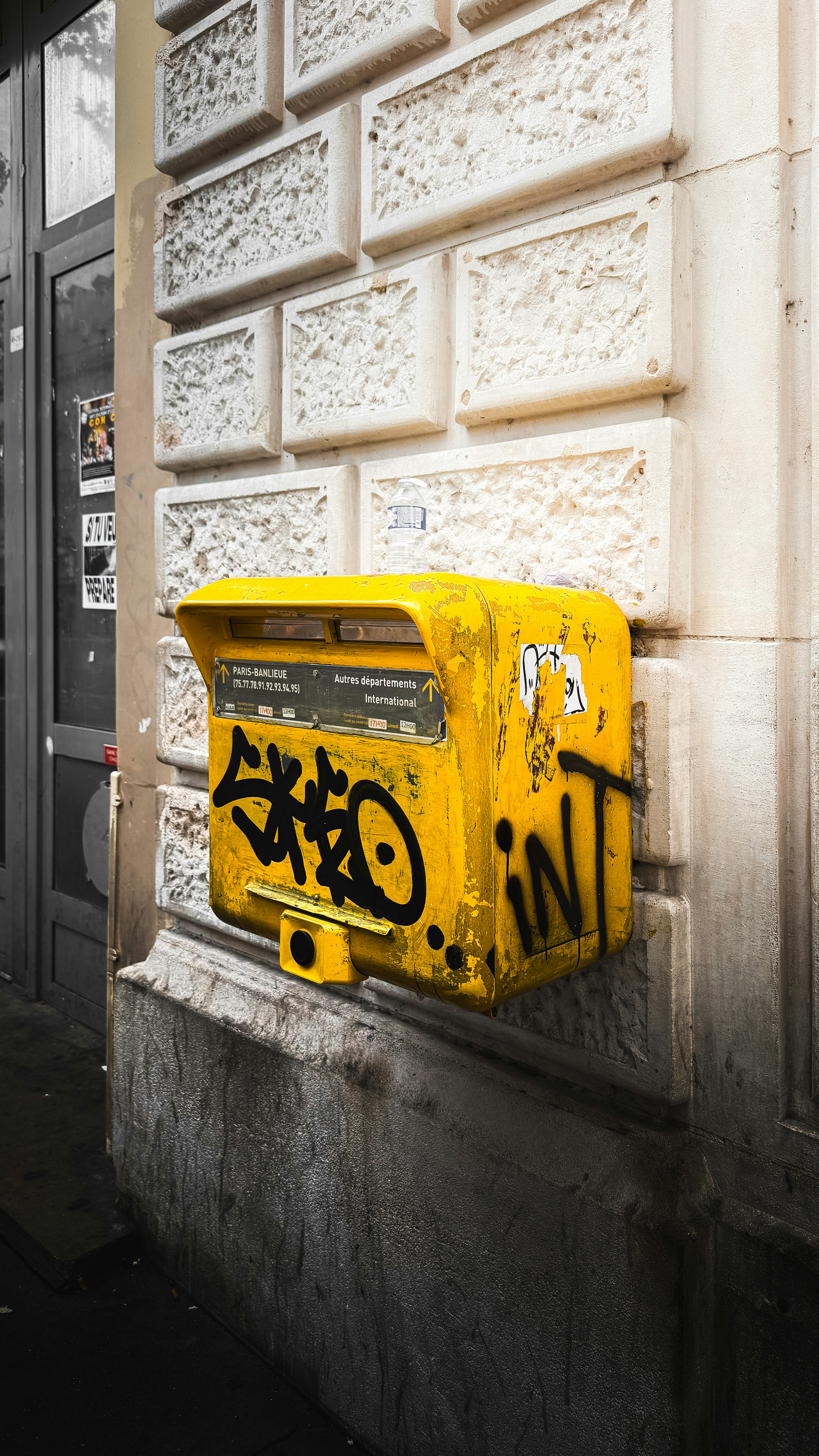 Yellow mailbox covered in graffiti on a building wall.