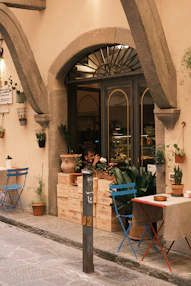 Outdoor cafe seating with potted plants and arched entrance.