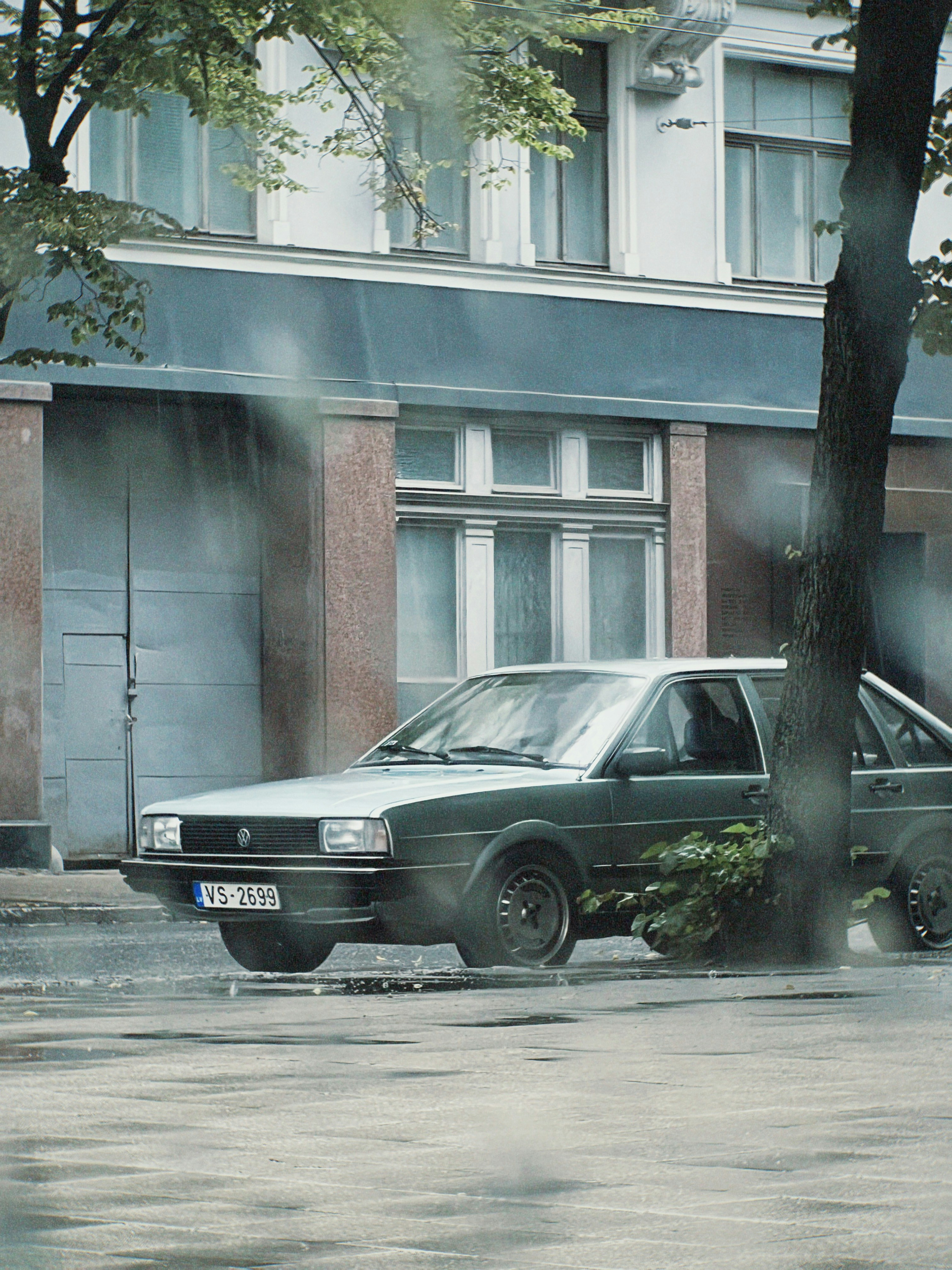 A vintage car parked on a wet street during rain.
