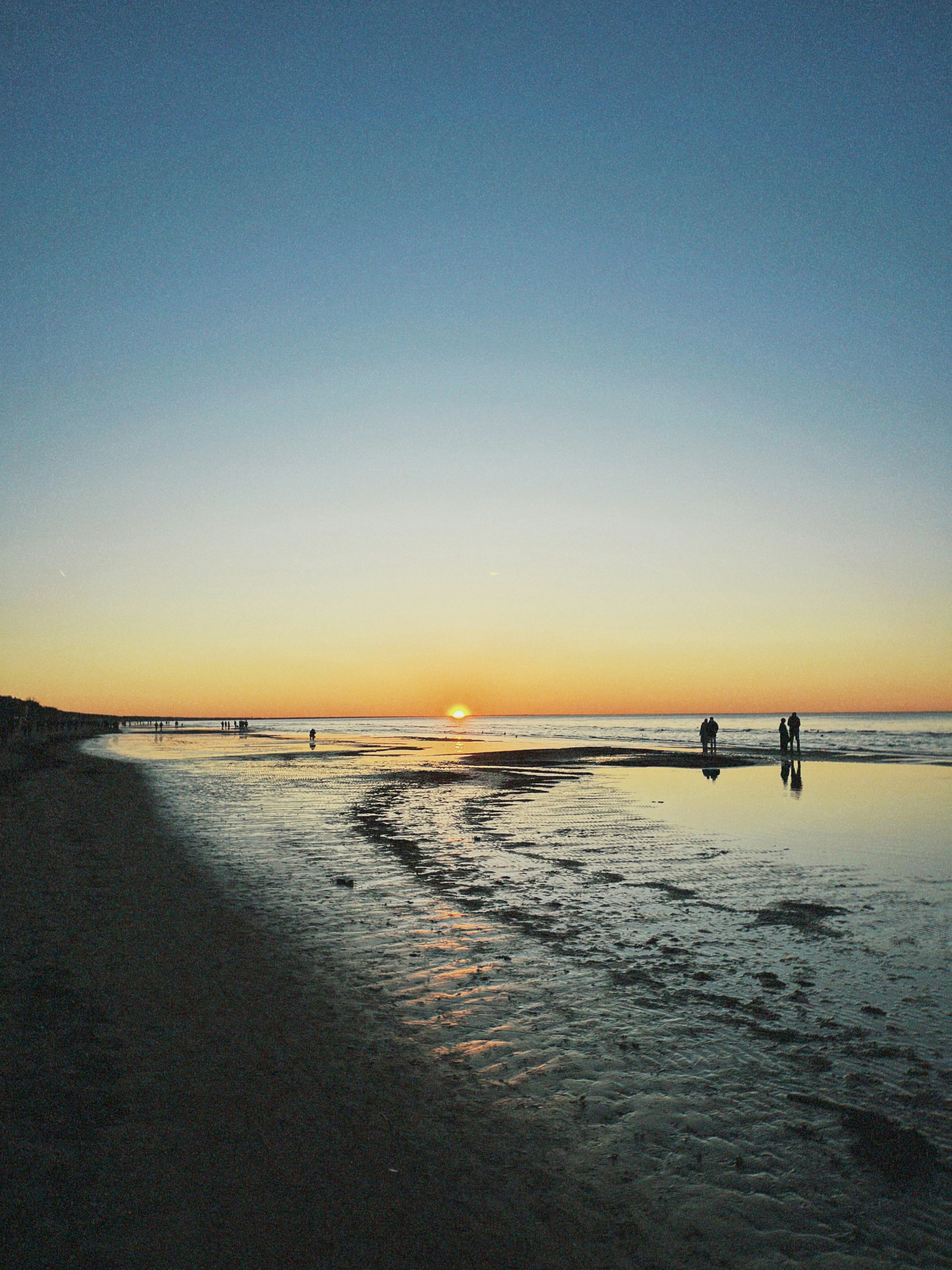 Sunset over a calm ocean with people walking