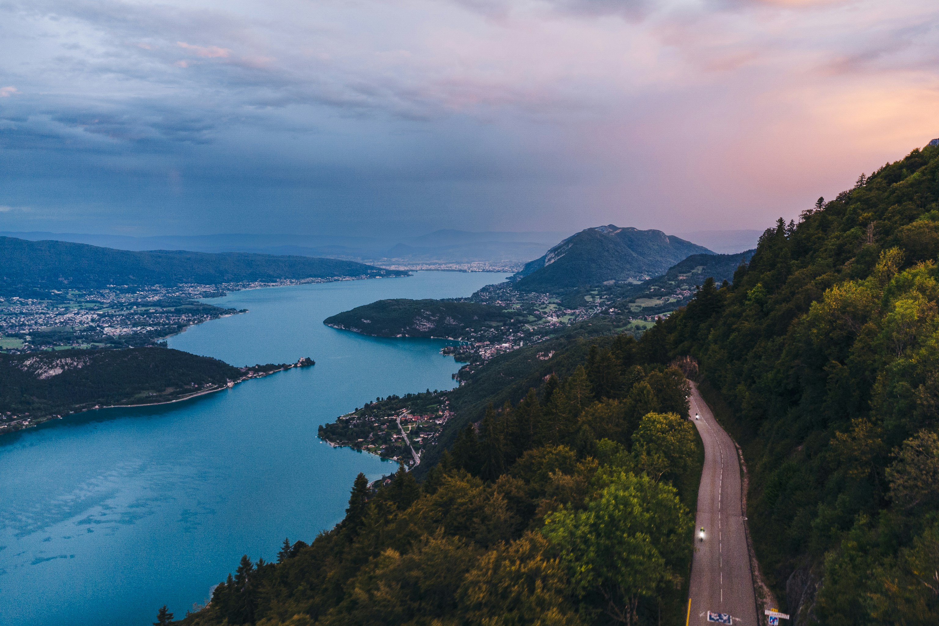 Winding road along a blue lake and forested mountains.