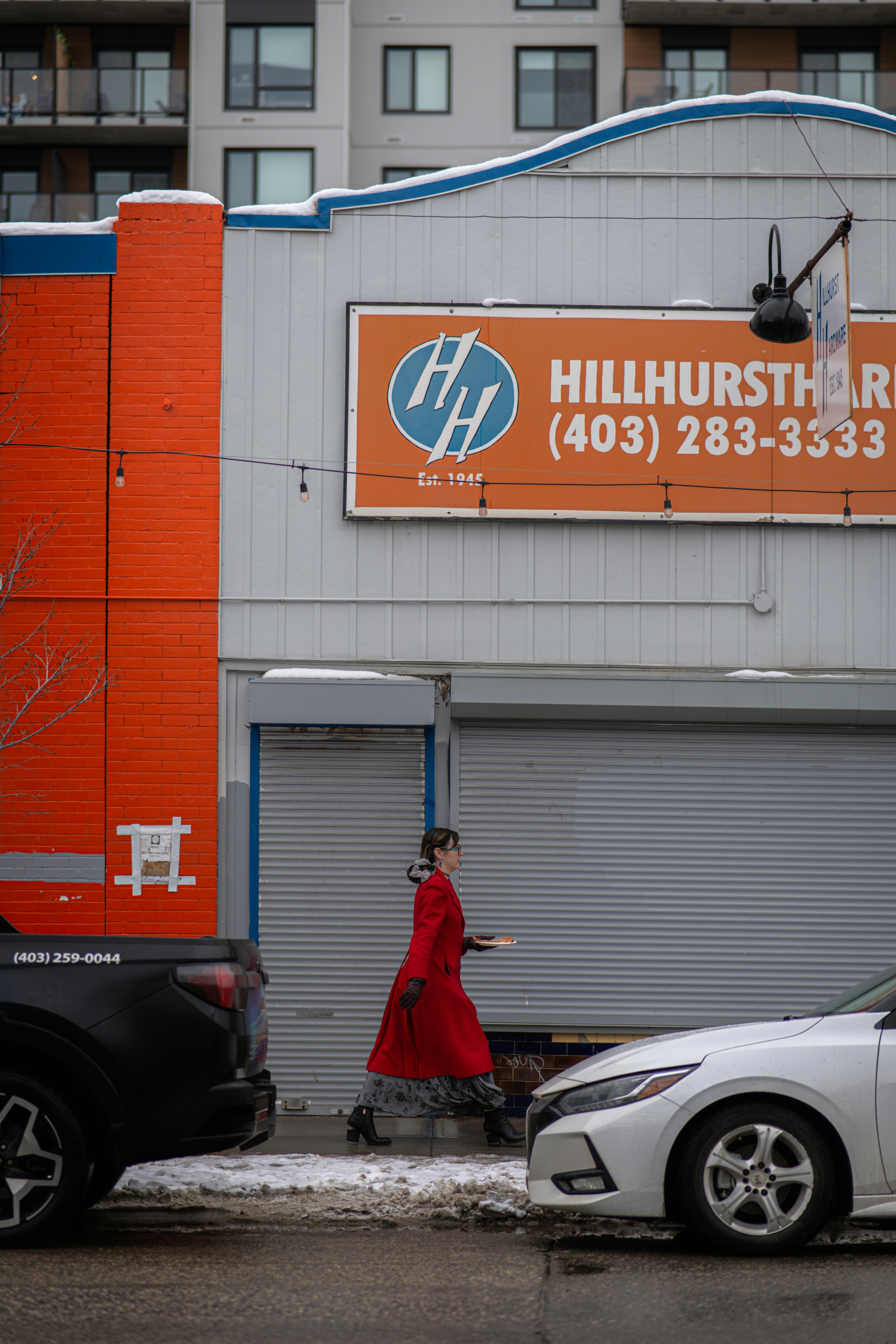 Woman in red coat walks past building with sign