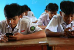 Students in uniform using smartphones in classroom.