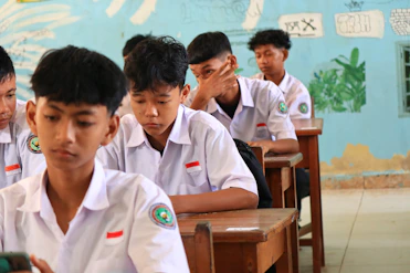 Students in white uniforms sitting at desks in classroom.