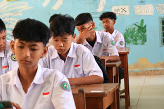 Students in white uniforms sitting at desks in classroom.