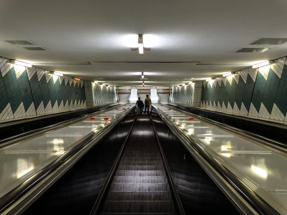Black and silver escalator system inside an underground tunnel with two individuals standing