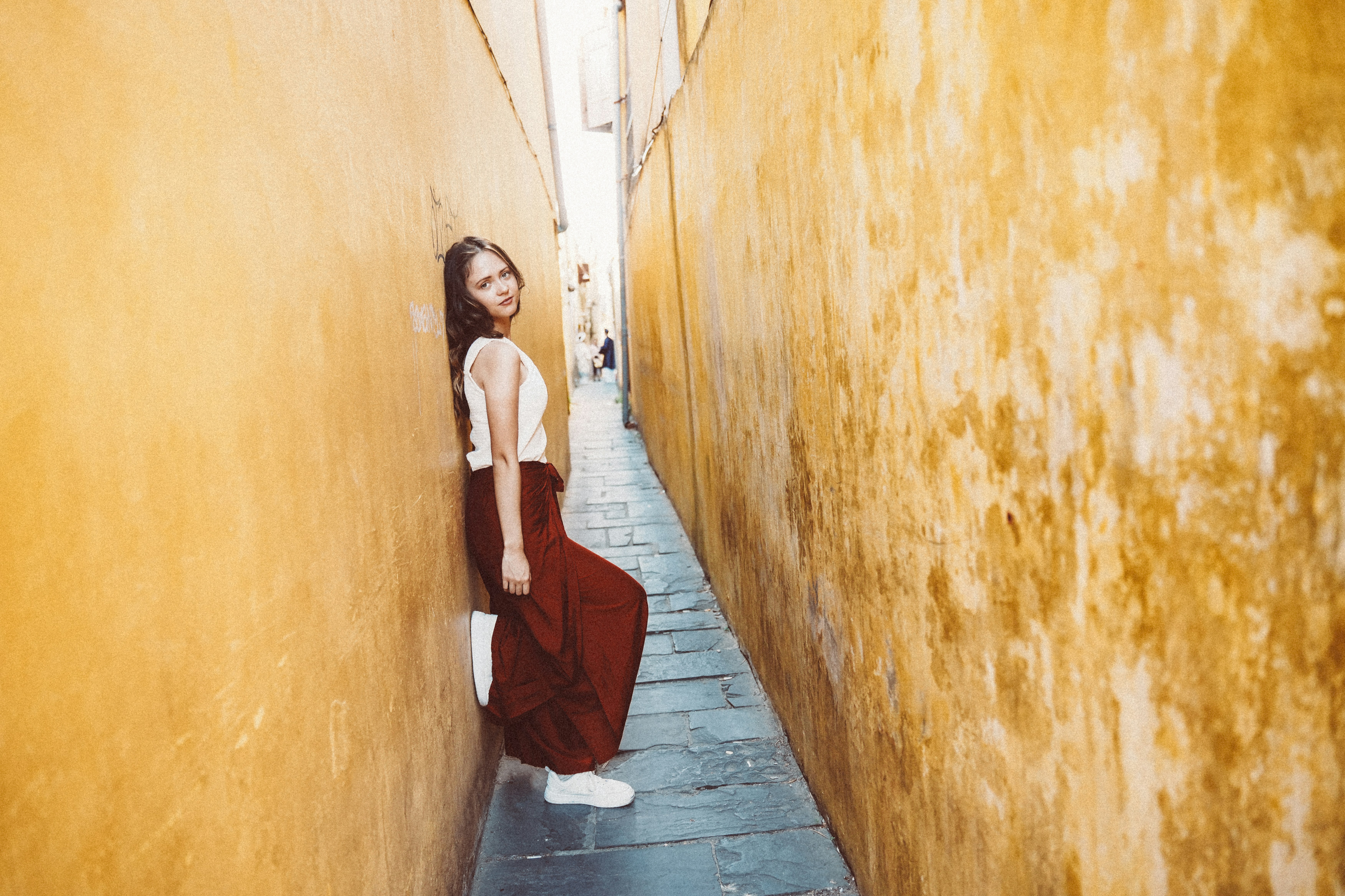 Young woman leaning against textured yellow wall in alley.