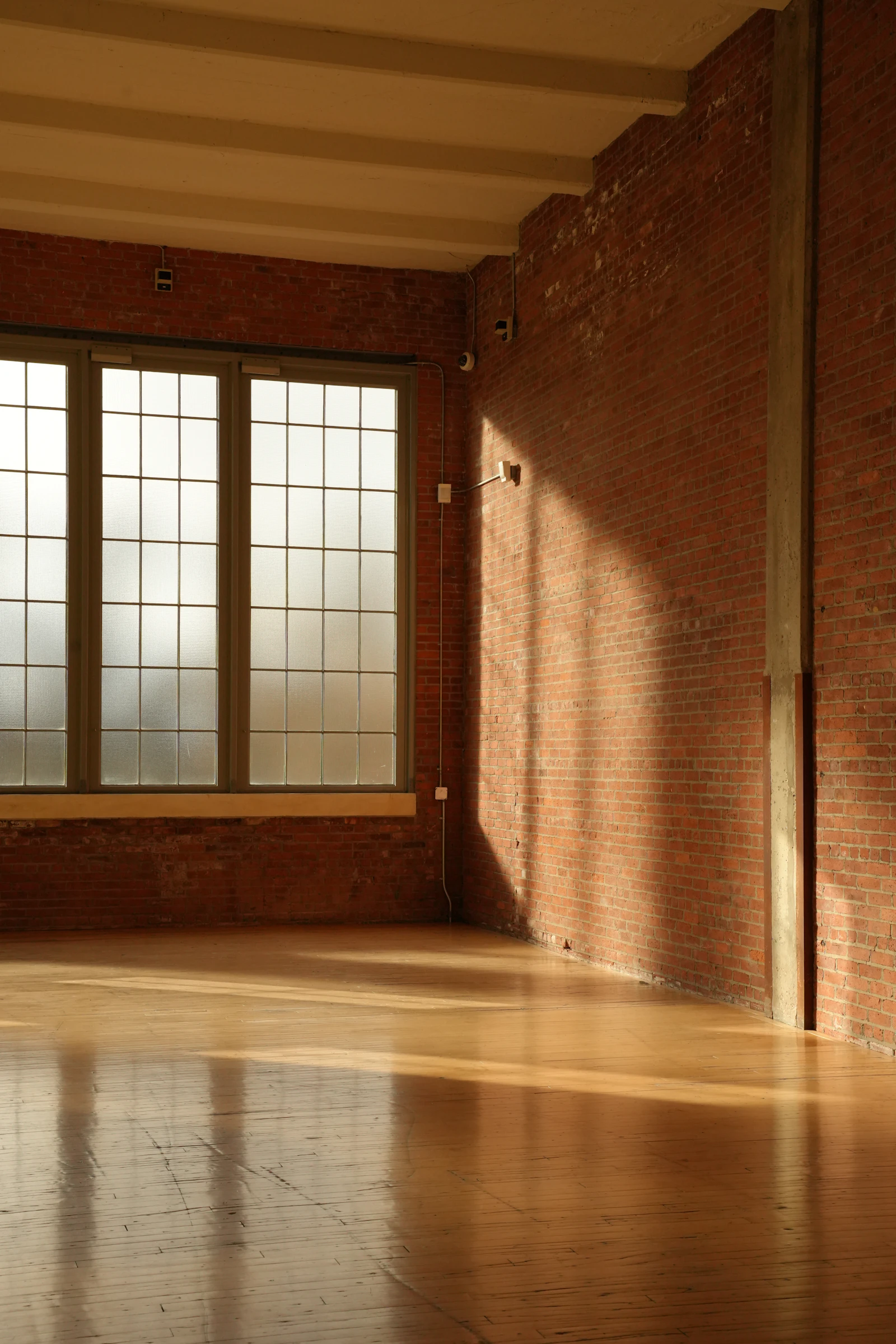 Großer Altbauraum mit Backsteinwand, Fensterfront und durchgehendem Holzboden
