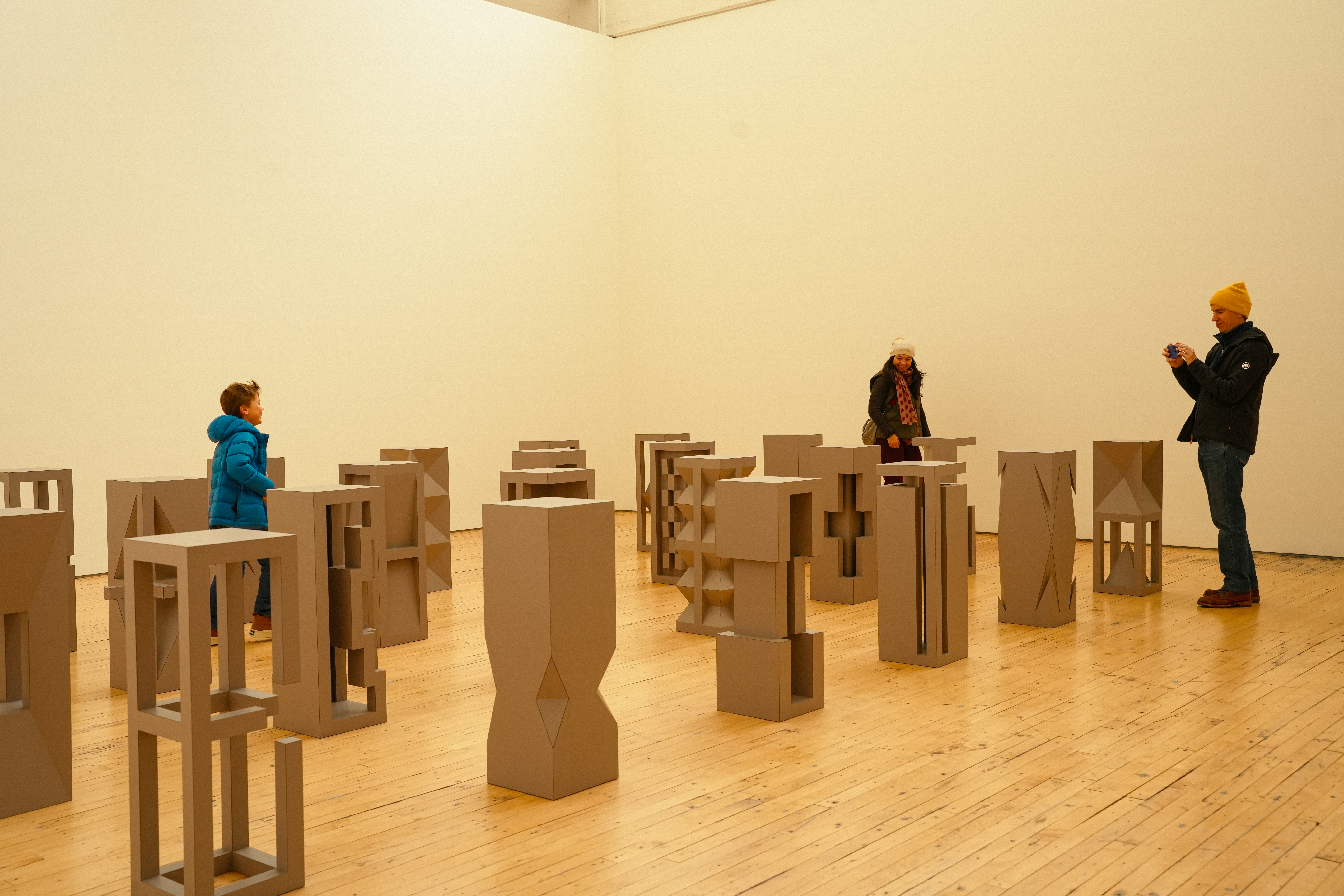 People observe abstract sculptures in a white gallery room.