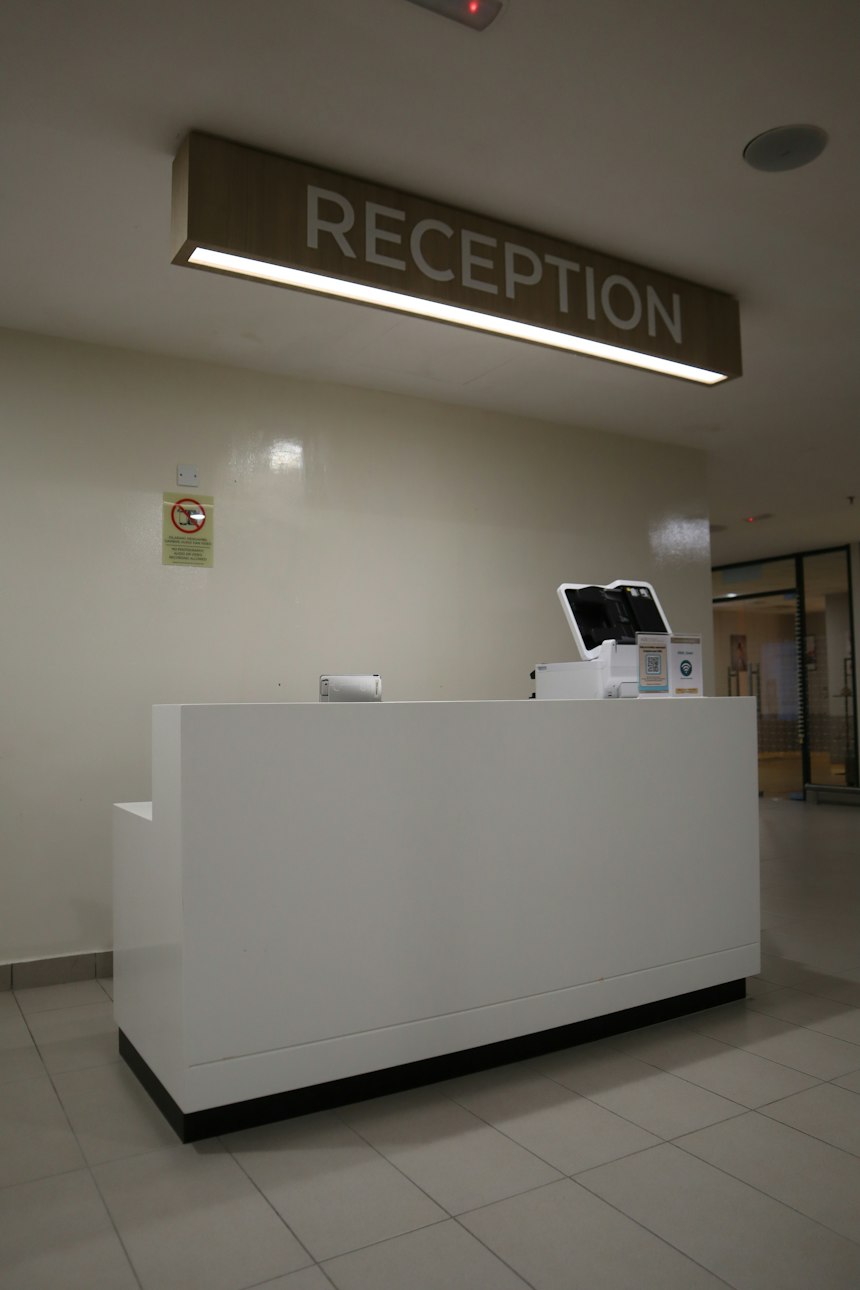 A modern clinic reception desk with a sign overhead and a clean, organized front desk workstation.
