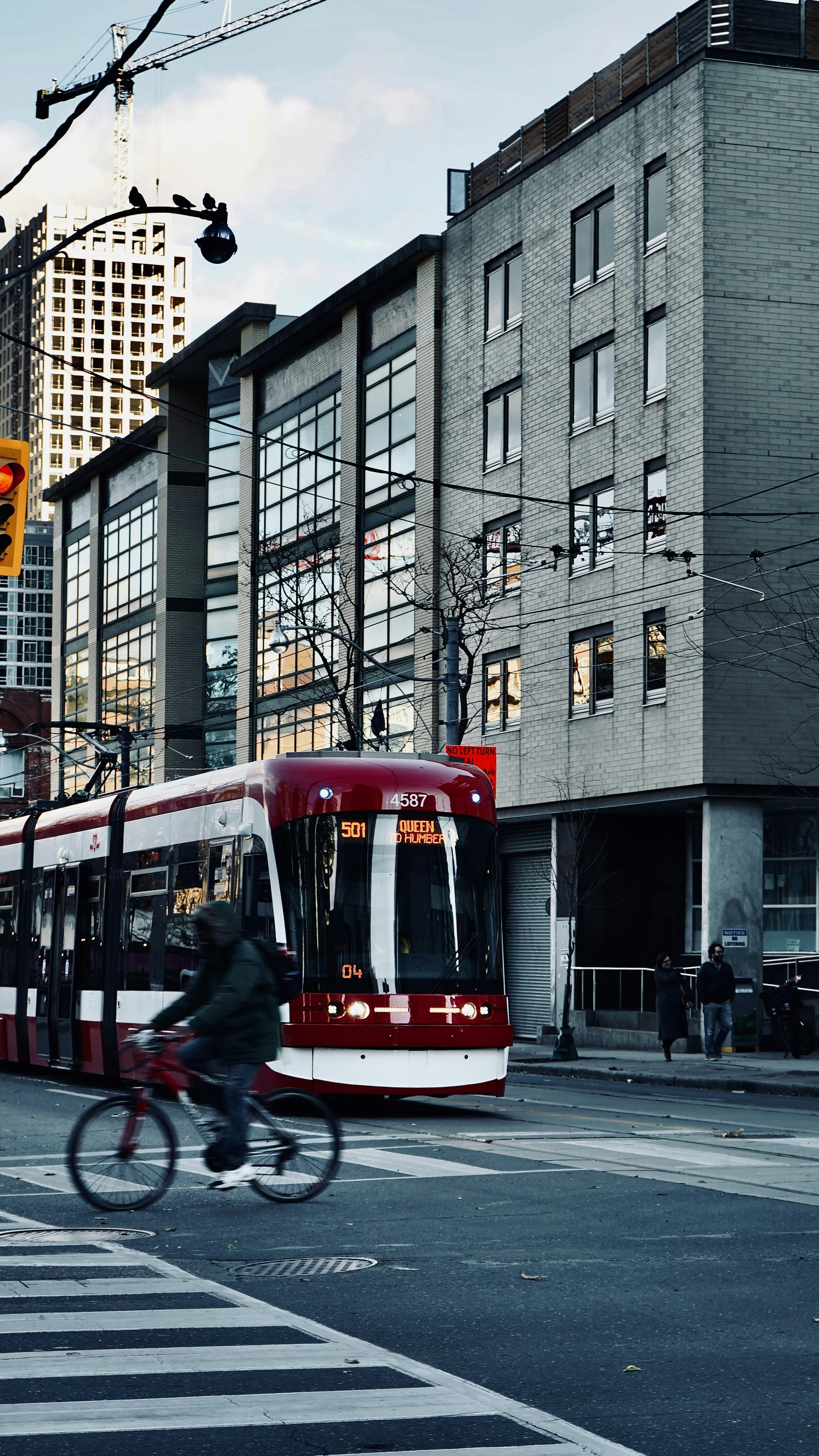 Red streetcar passes cyclist on city street crossing