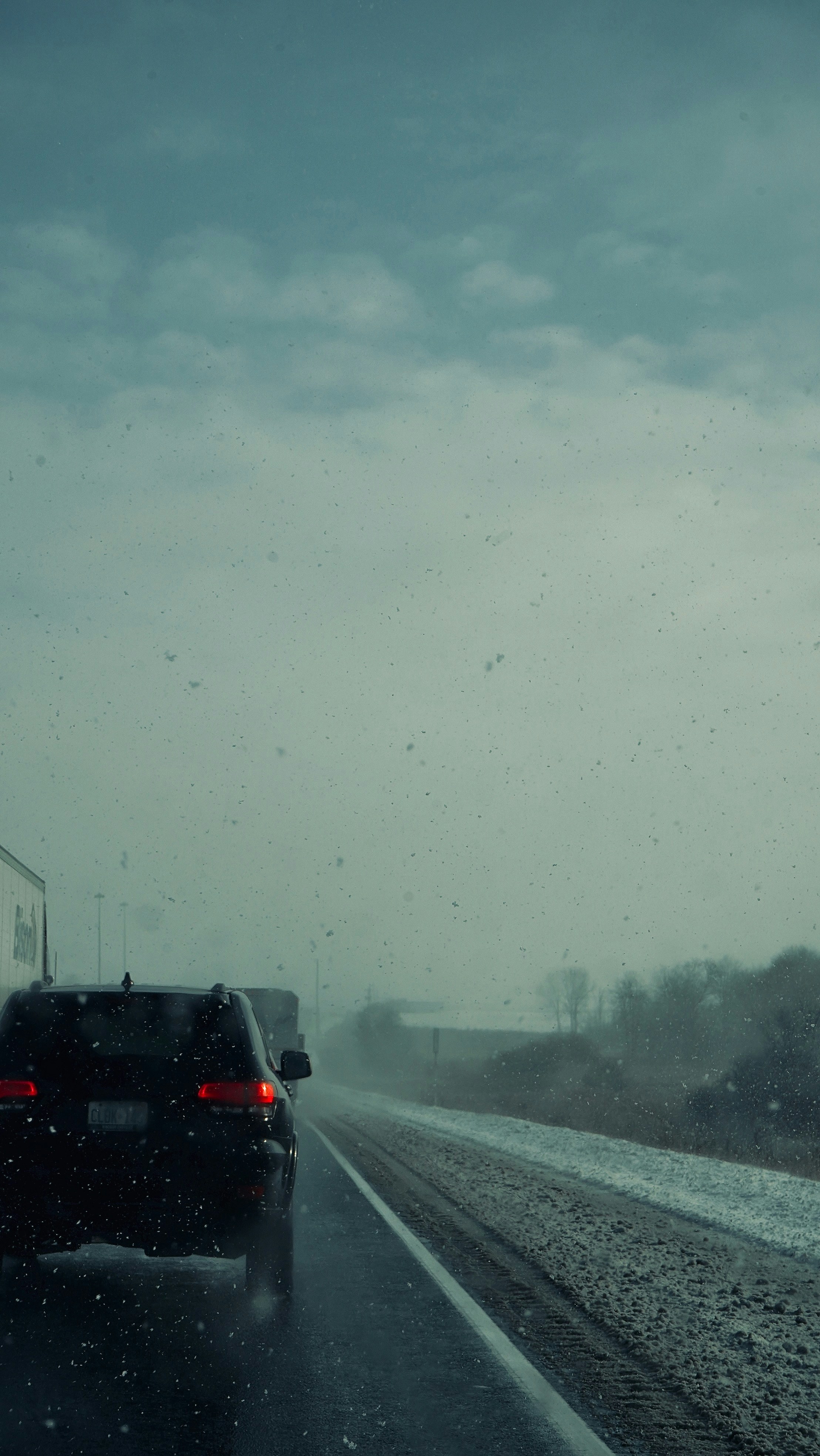 Cars driving on a wet road during a snowstorm.