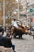 Charging bull statue on cobblestone street with onlookers