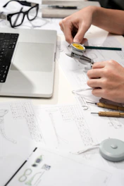 Hands measuring watch part with calipers and blueprints