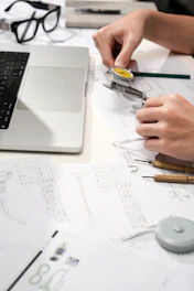Hands measuring watch part with calipers and blueprints
