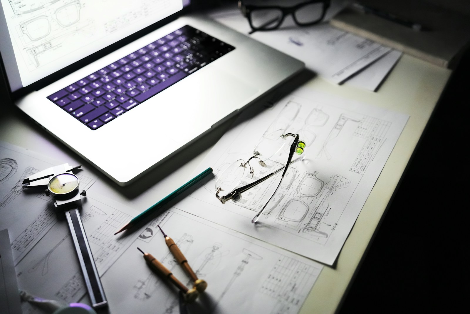 Plans techniques, ordinateur portable et outils de mesure posés sur le plan de travail d'un bureau d'études