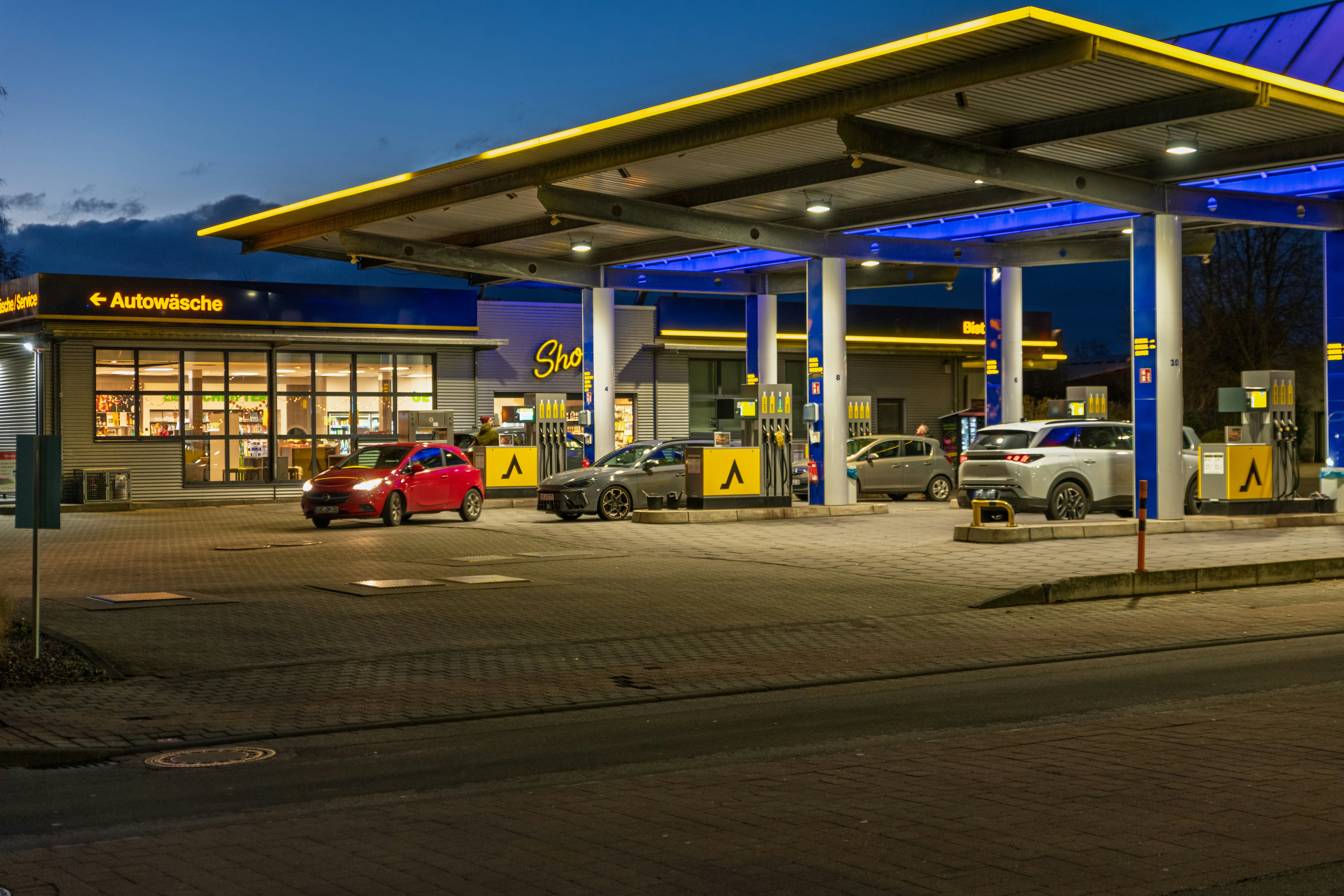Cars at a brightly lit gas station at dusk