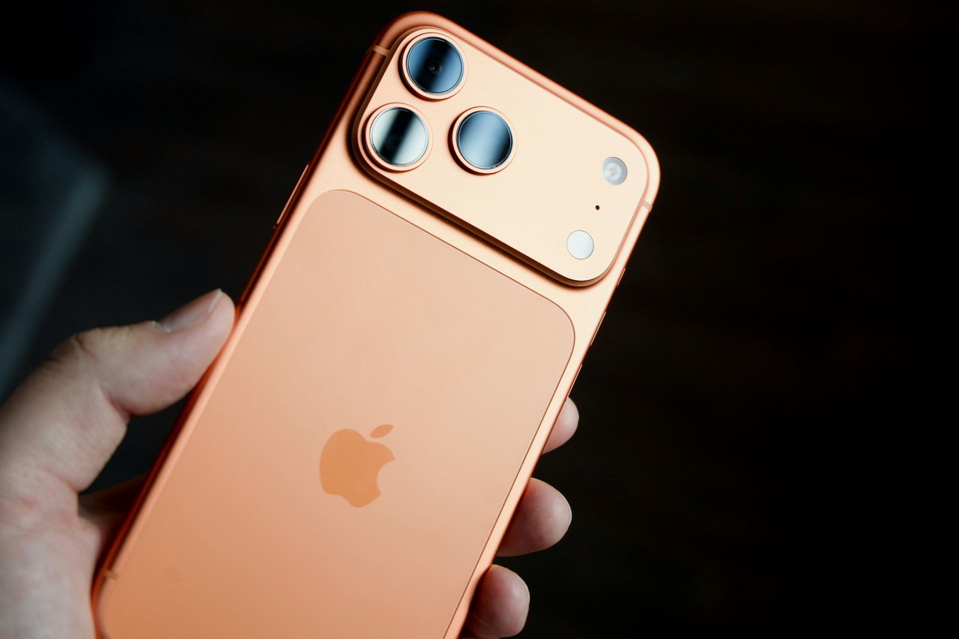Hand holding a rose gold smartphone with triple camera.