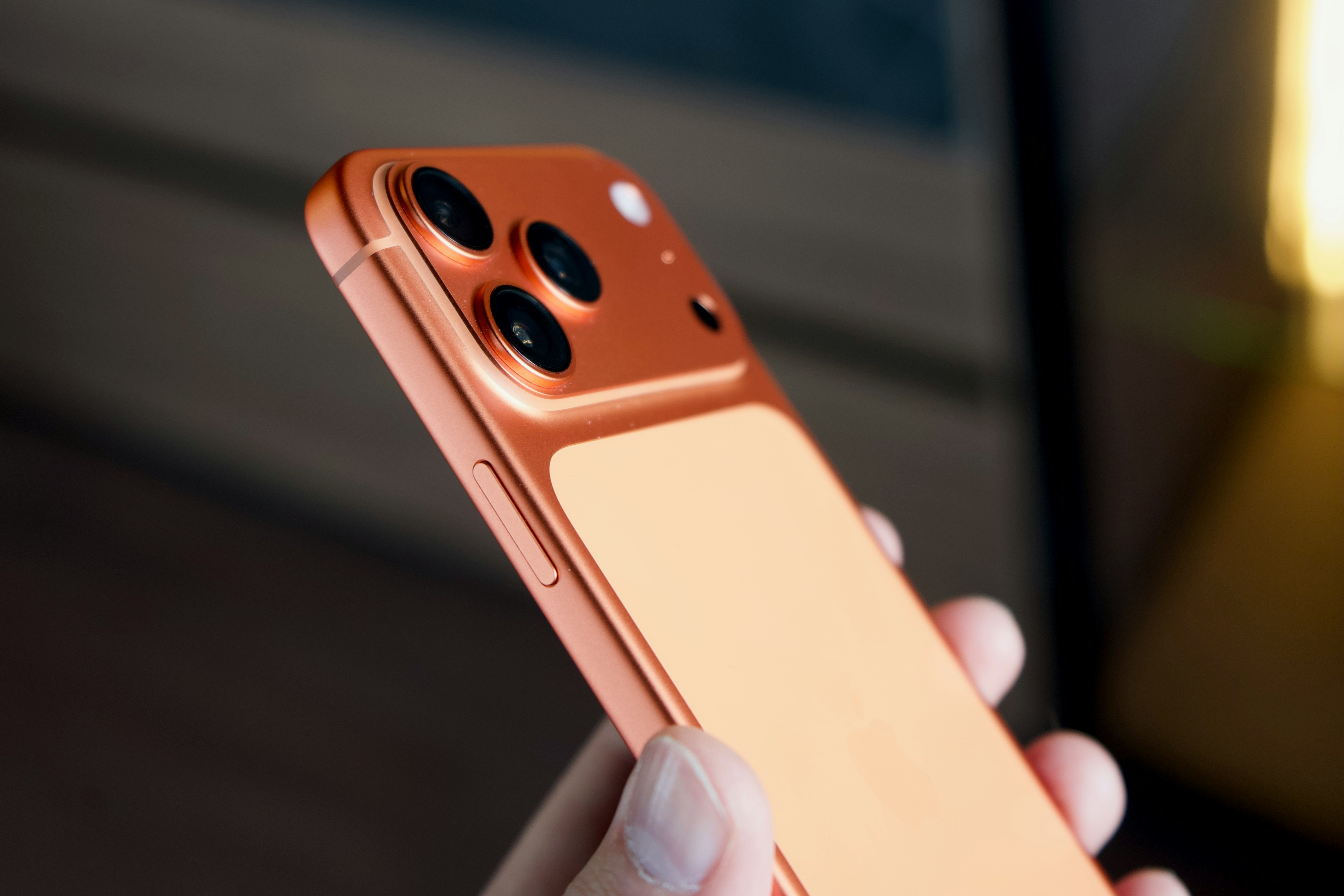 Smartphone arancione con tripla fotocamera tenuta a mano