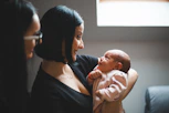 Mother holding her newborn baby with another woman watching