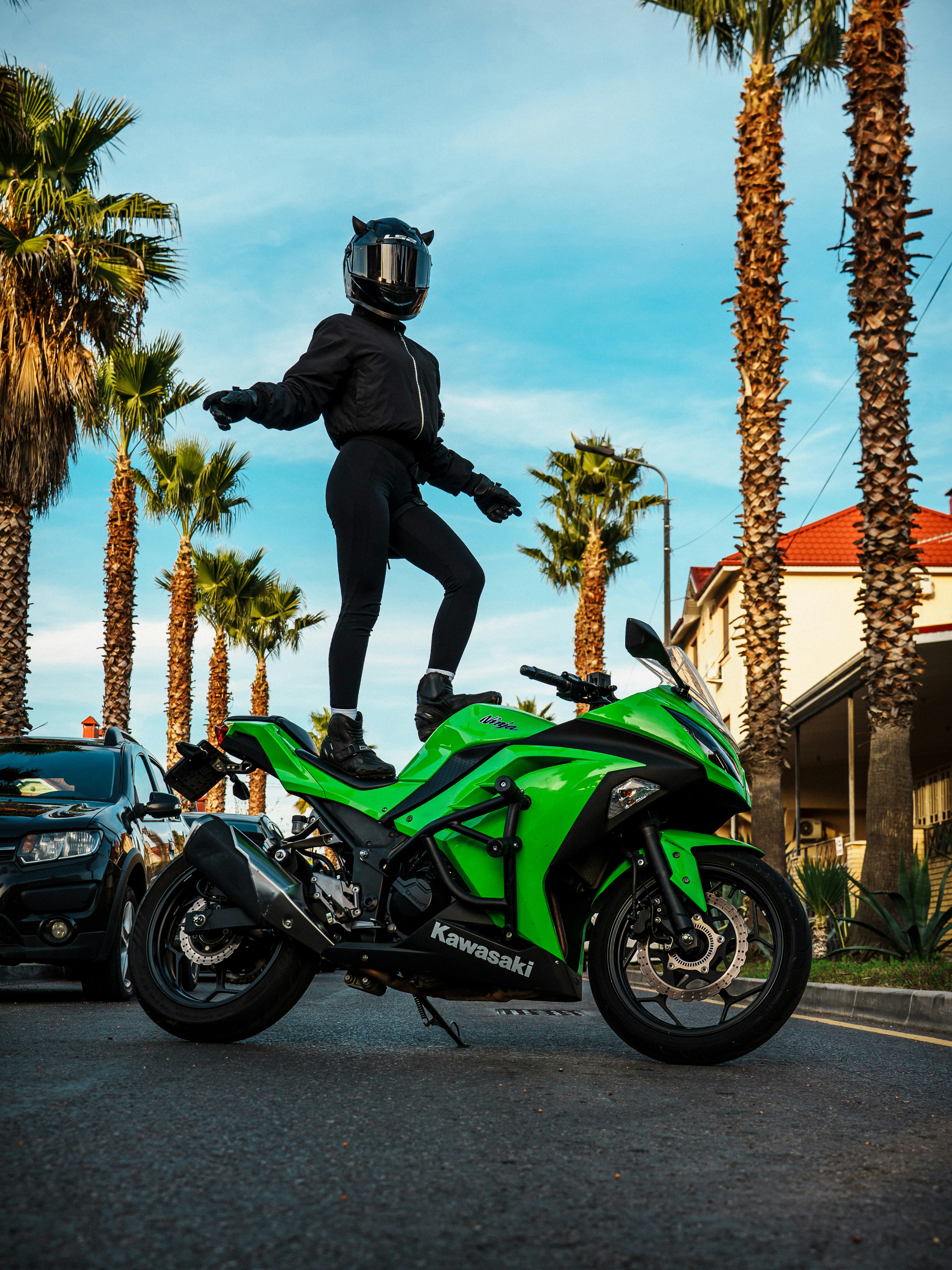 Woman in helmet standing on green motorcycle with palm trees.