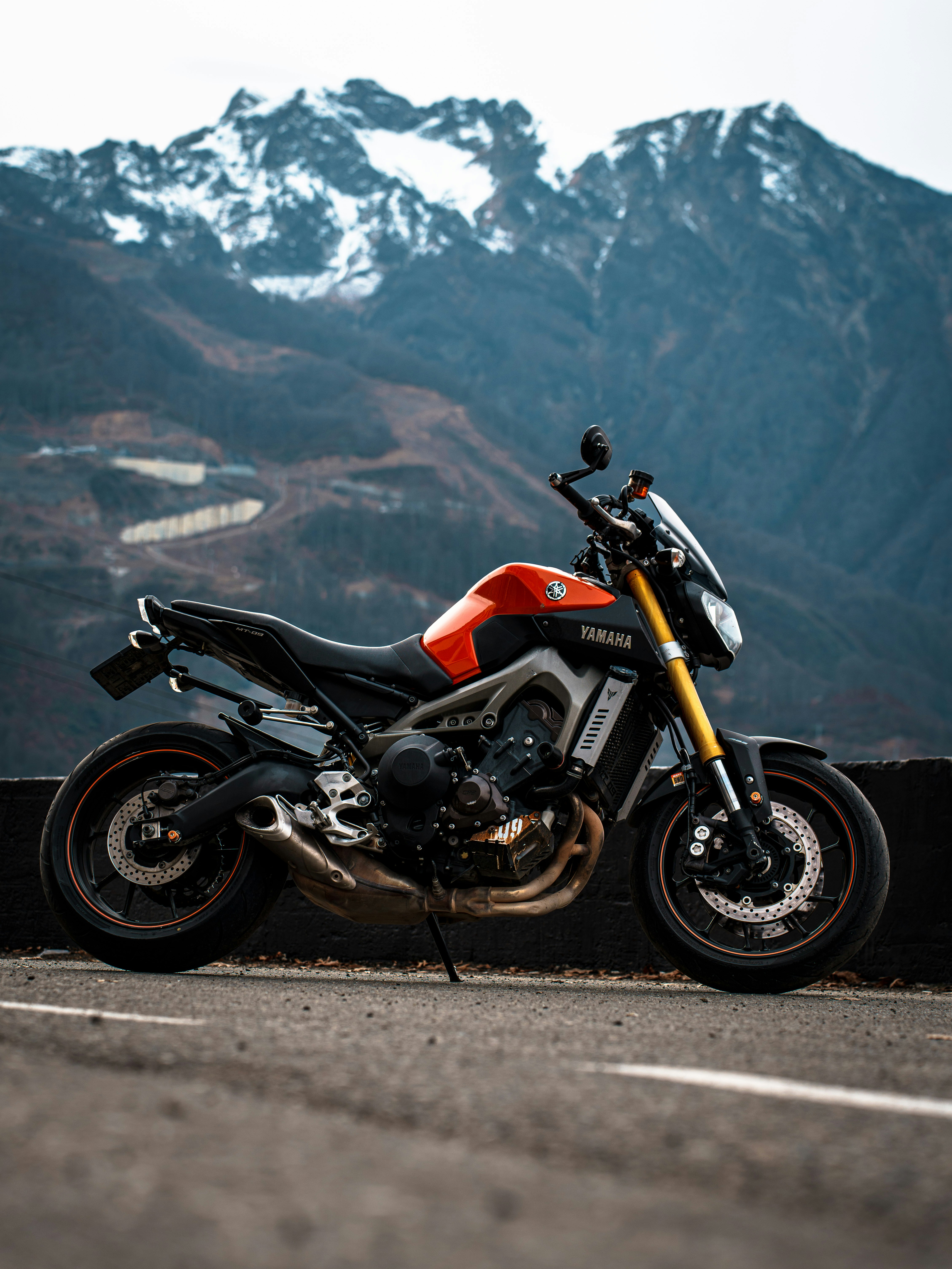 Orange motorcycle parked on asphalt with mountains behind