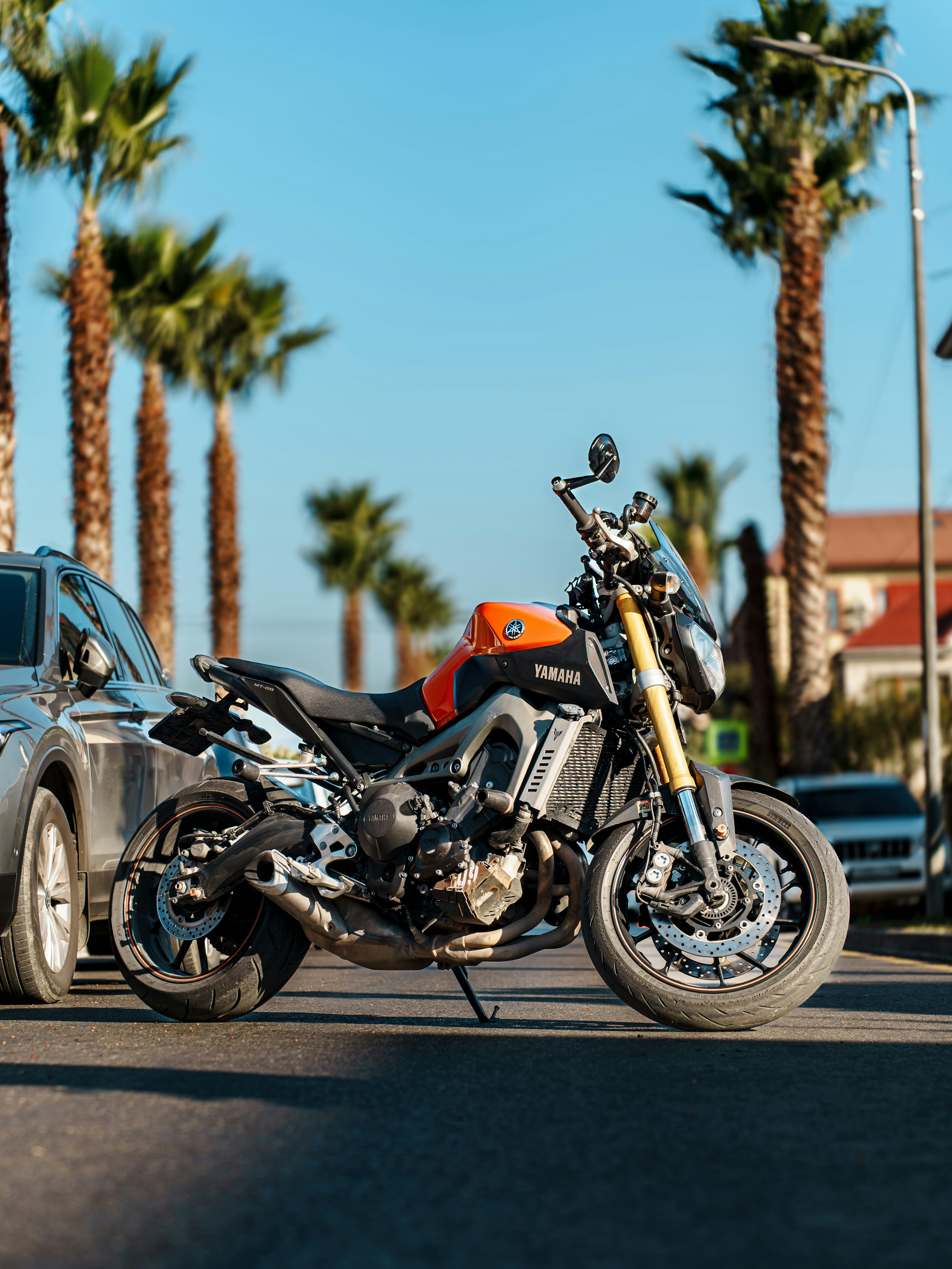Orange and black motorcycle parked on street with palm trees