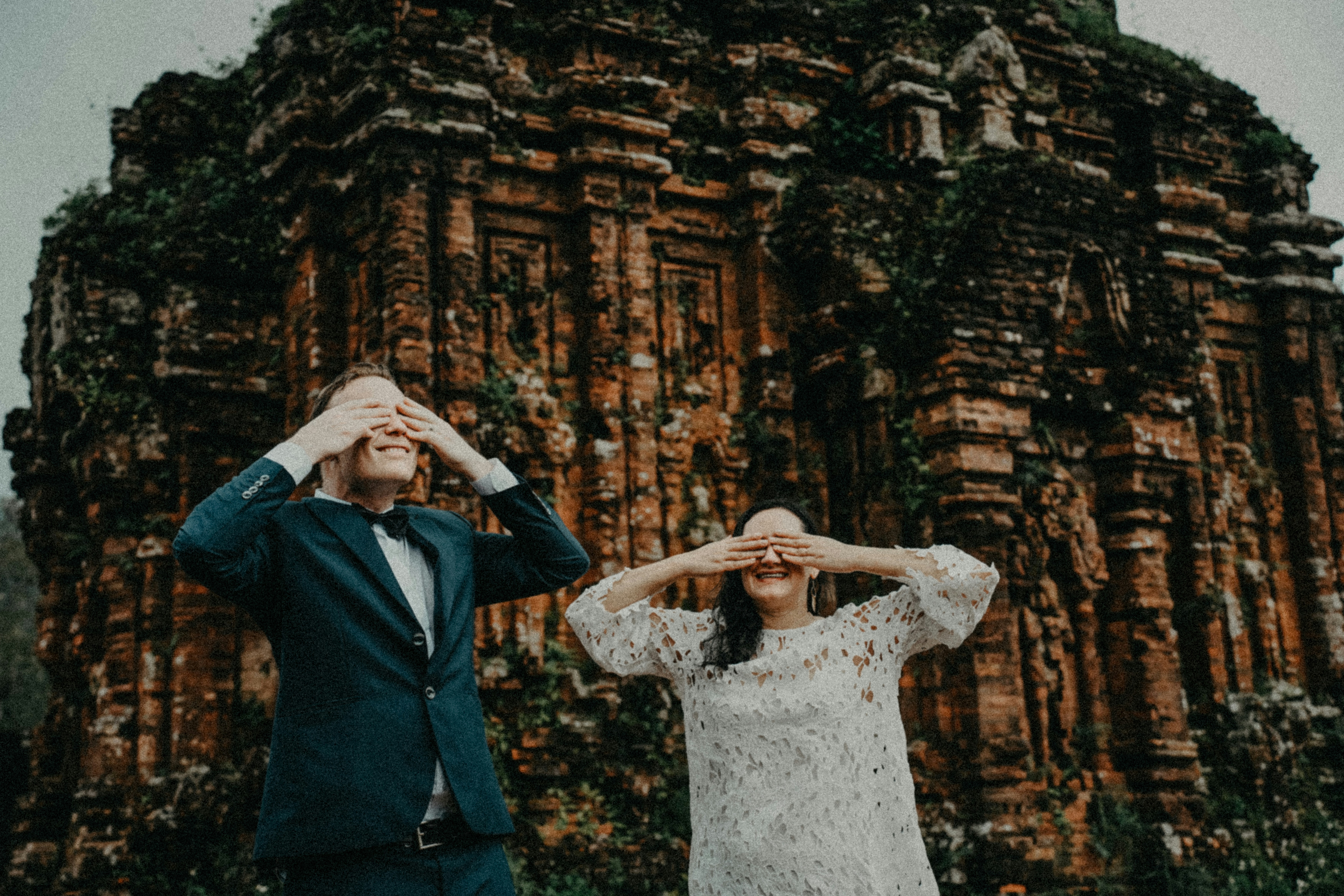 Couple covers eyes in front of ancient brick ruins.
