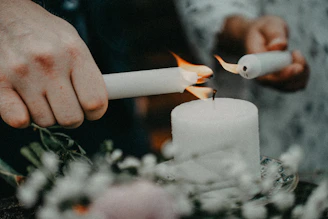 Hands lighting a white candle with a lighter.