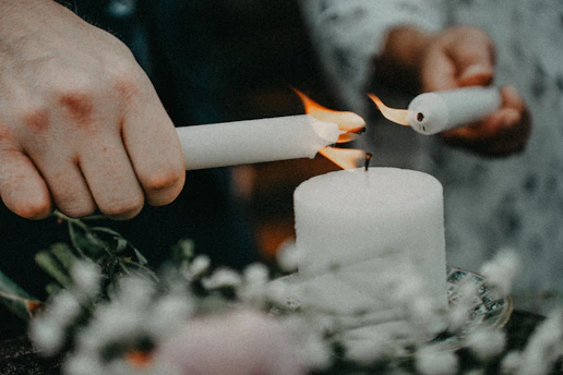 Hands lighting a white candle with a lighter.