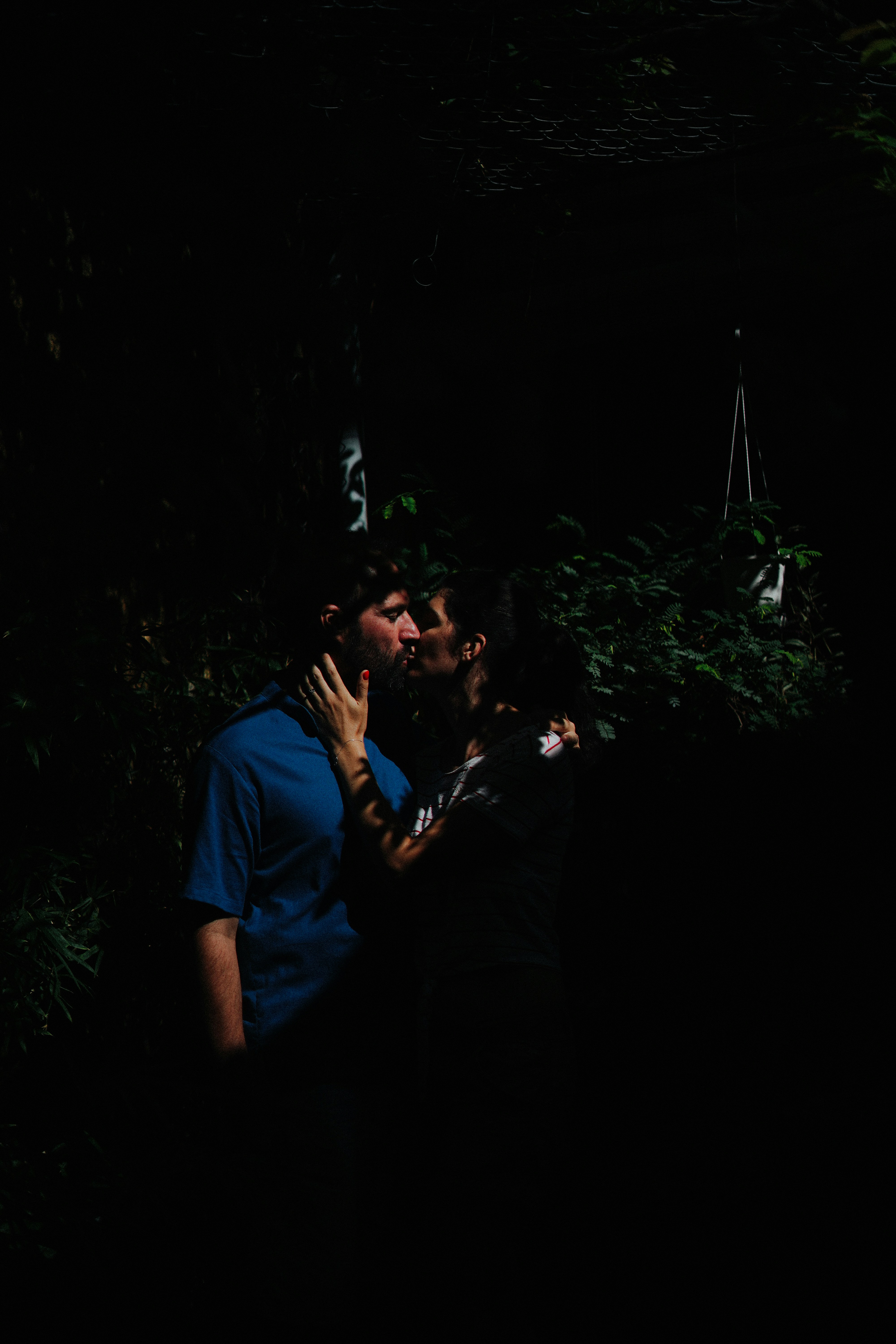 Couple kissing amidst dark foliage