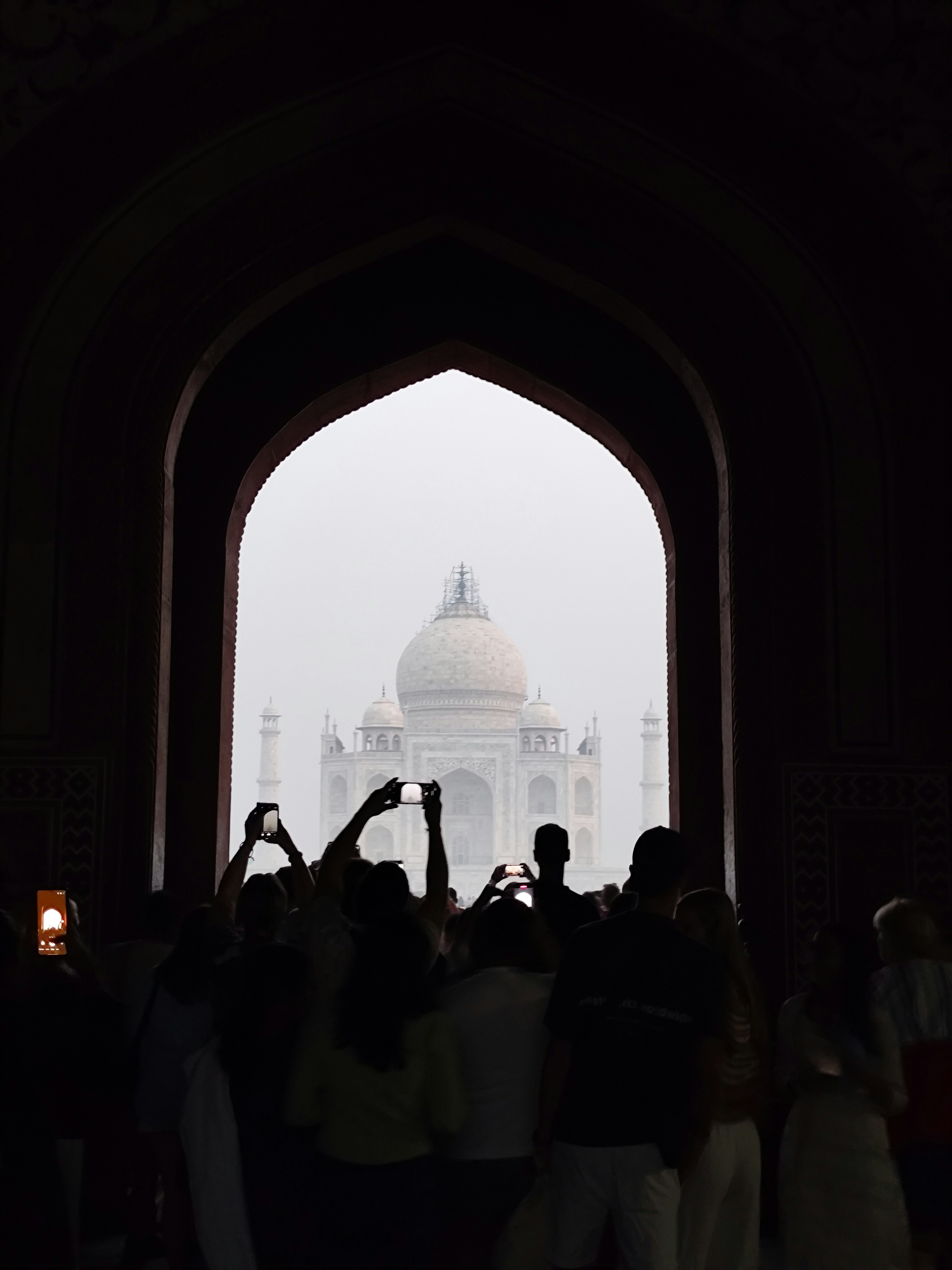 People taking photos of taj mahal through an archway.