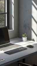 Laptop, keyboard, and mouse on a desk with sunlight.