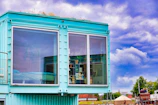 Modern turquoise shipping container home with large windows.