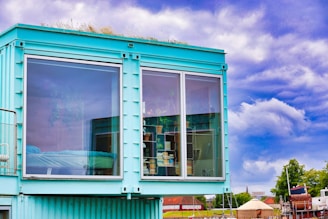Modern turquoise shipping container home with large windows.