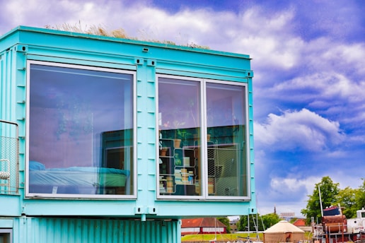 Modern turquoise shipping container home with large windows.