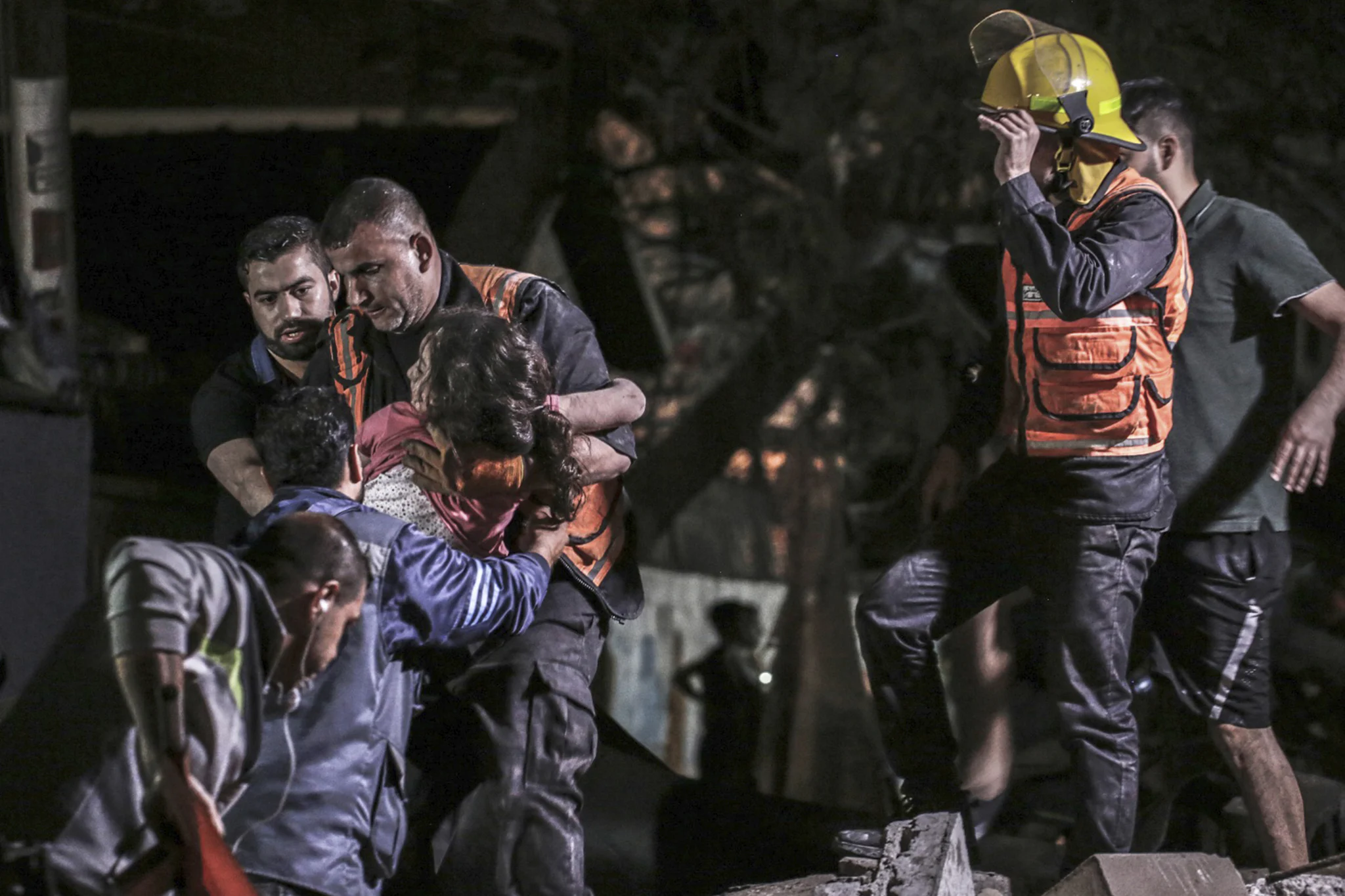 Civil defence workers carry a child rescued from the rubble in Gaza at night
