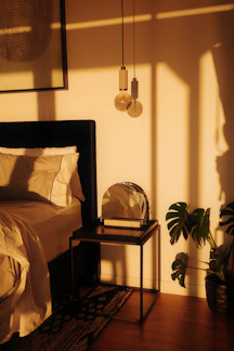 Warm light illuminates a bedroom with a bed and plant.