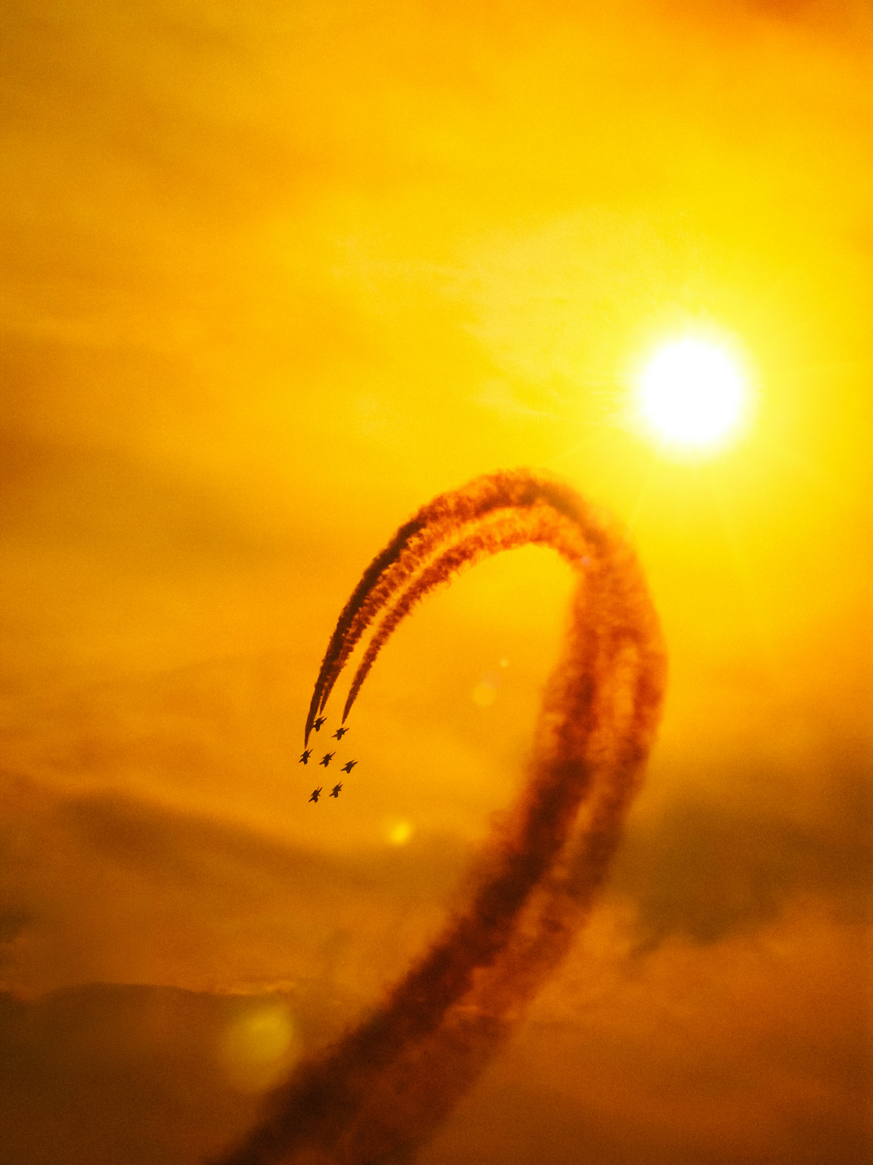 Planes create smoke trails against a bright sun.